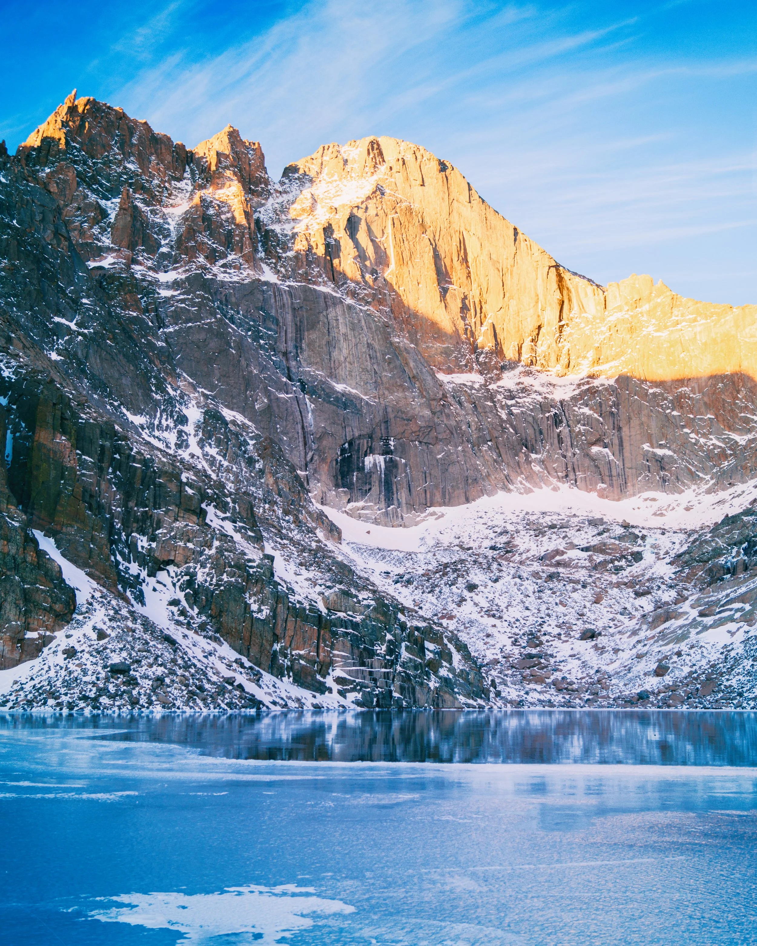 Snow-covered mountain near a frozen lake with a clear blue sky.
