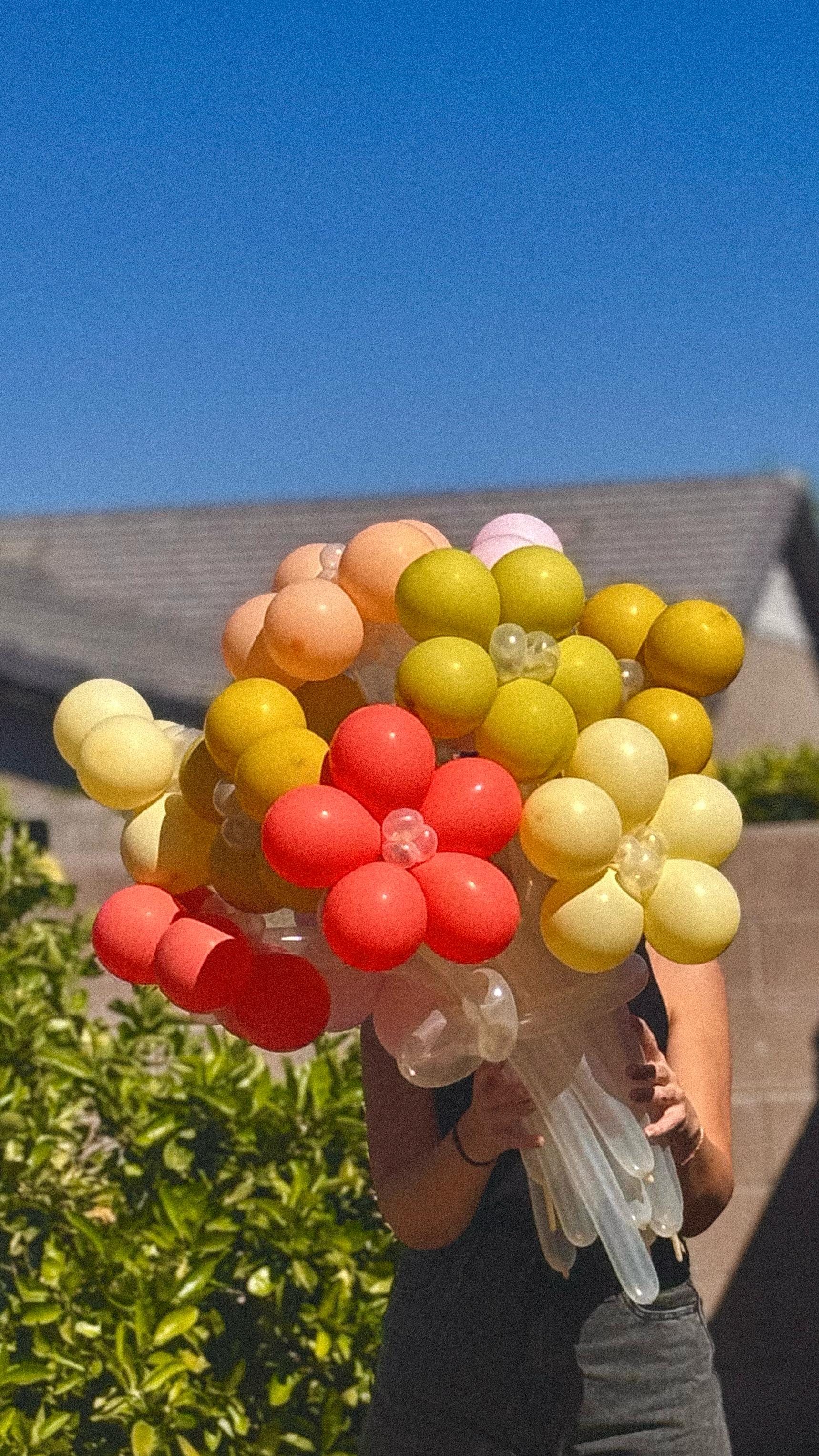 Person holding a bouquet of colorful balloon flowers with a clear blue sky in the background.