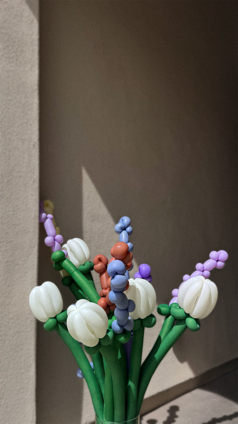 Beaded floral bouquet made of colorful beads, shaped like flowers with green stems and white petals, set against a shadowed background.
