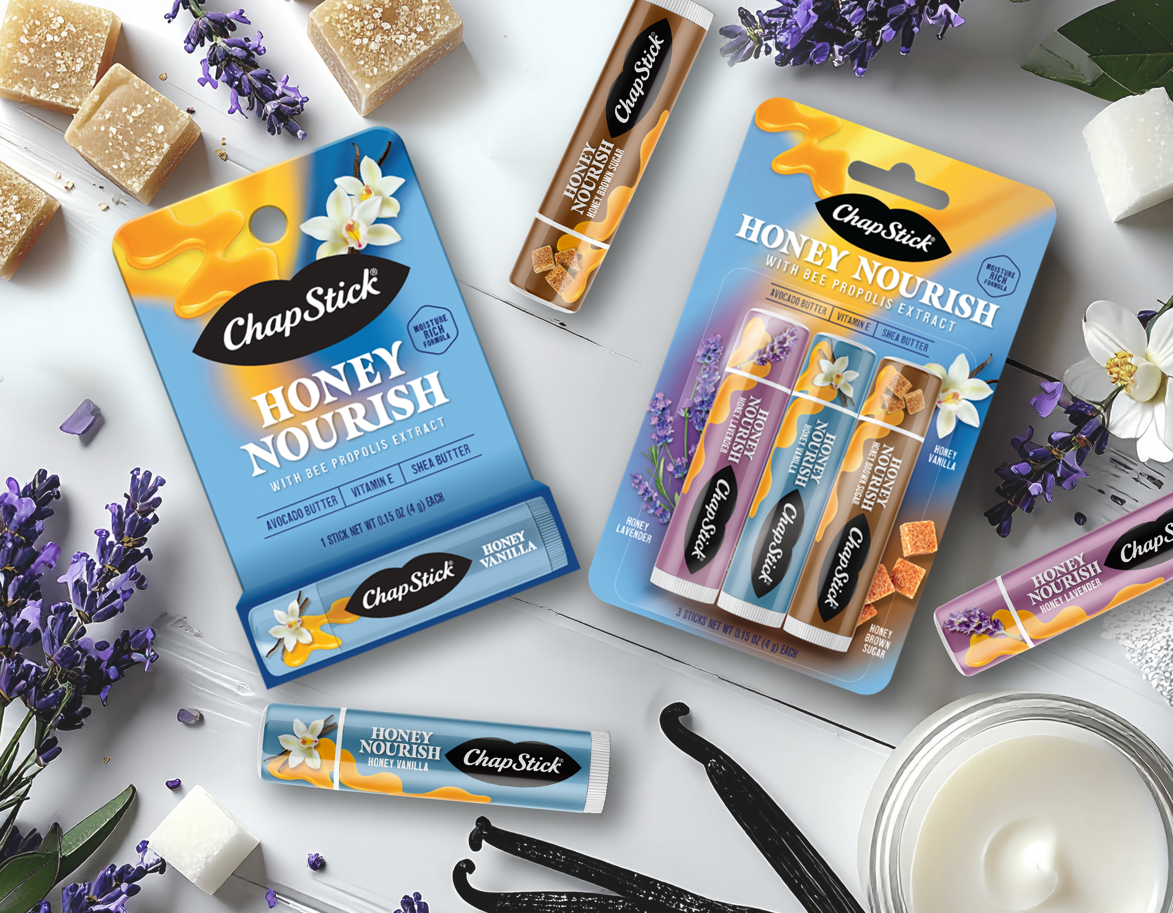 Assorted ChapStick lip balm products in honey nourish flavors with natural ingredients displayed on a white surface with purple lavender flowers, vanilla beans, and chunks of soap and sugar cubes.