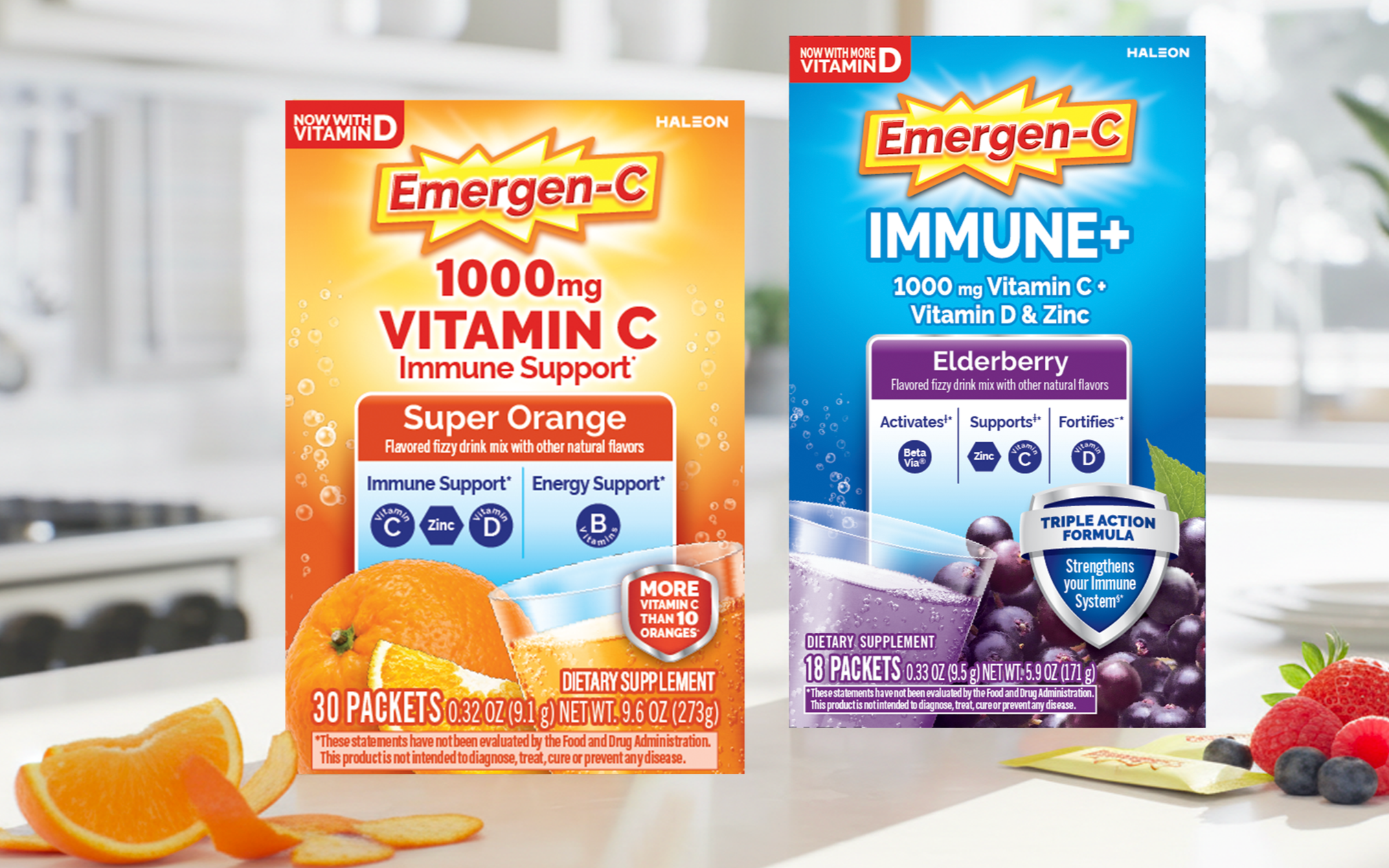 Two boxes of Emergen-C dietary supplements, one orange flavored and one elderberry flavored, on a kitchen countertop with fruit and a packet of blueberries beside them.