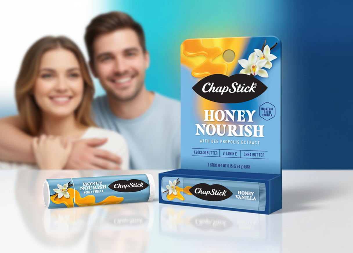 A smiling young couple, a woman with brown hair and a man with brown hair, sitting behind a table with two ChapStick lip balm products, one in a stick container labeled "Honey Vanilla" and one in a box labeled "Honey Nourish" with ingredients like avocado butter, vitamin E, and shea butter, featuring a honey swirl and a vanilla flower on the packaging.
