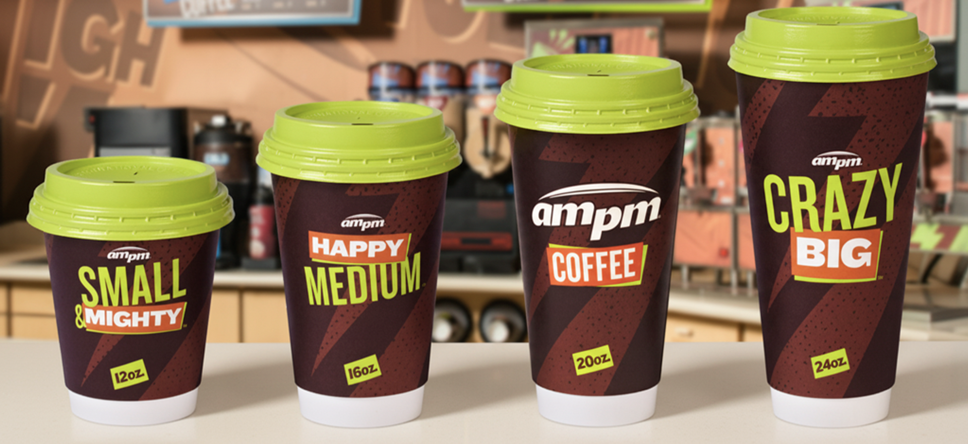 Four coffee cups of varying sizes on a counter, labeled as small, medium, coffee, and crazy big, from left to right, with bright green lids and dark brown cups with red, yellow, and white text.