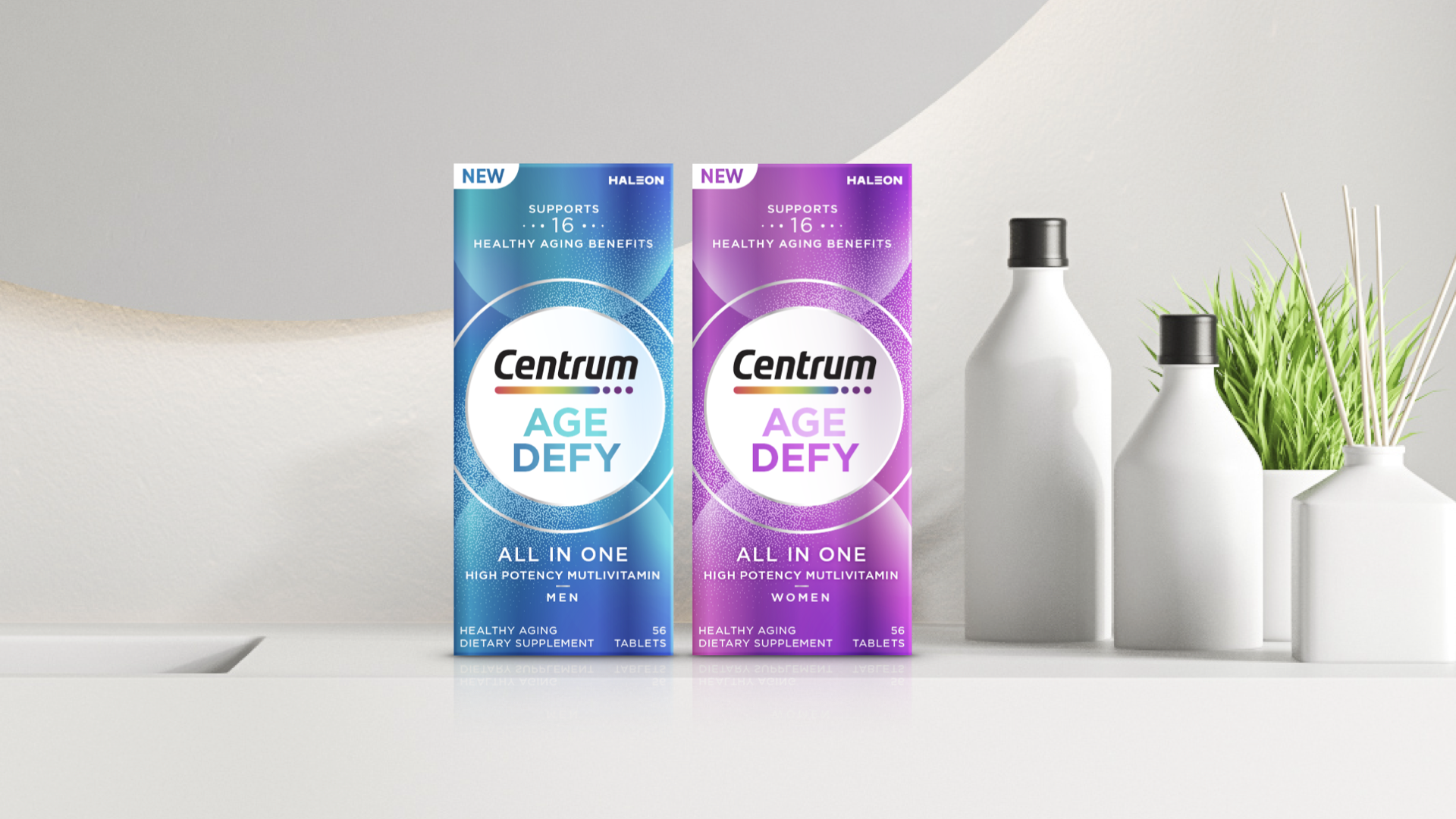 Two boxes of Centrum Age Defy multivitamins, one for men in blue packaging and one for women in purple packaging, placed on a white surface with white bottles and green plants in white vases in the background.