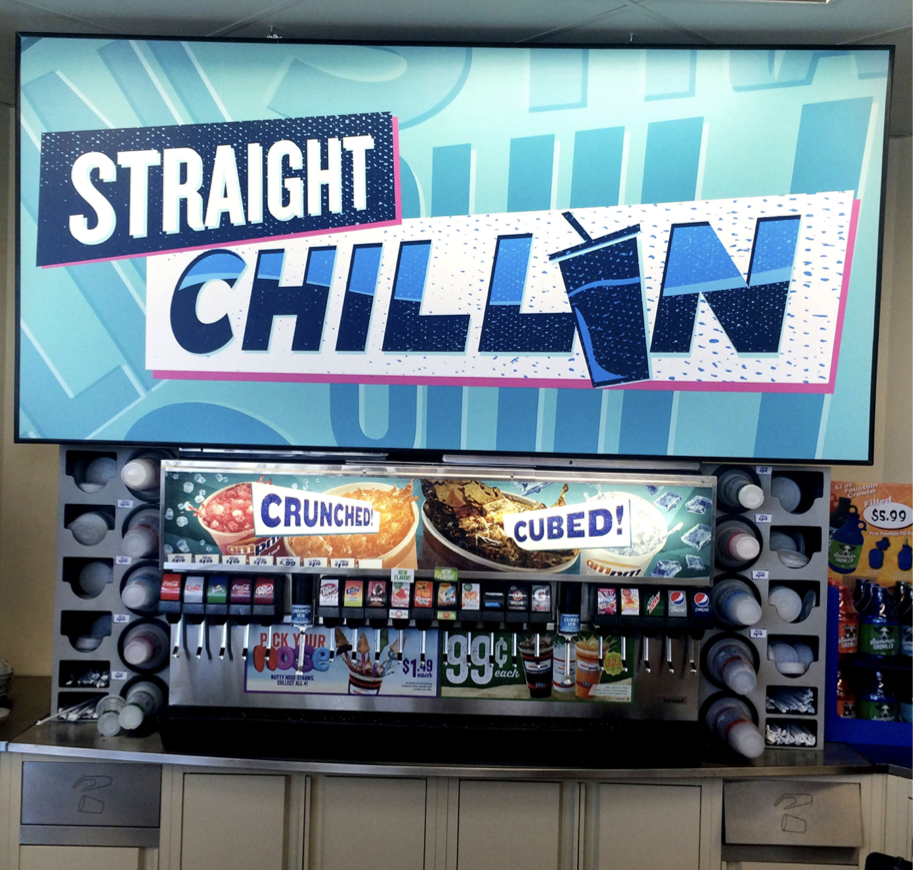 A drink dispenser at a convenience store featuring cups and beverage options with a sign reading 'Straight Chillain' and advertisements for crushed and cubed ice.