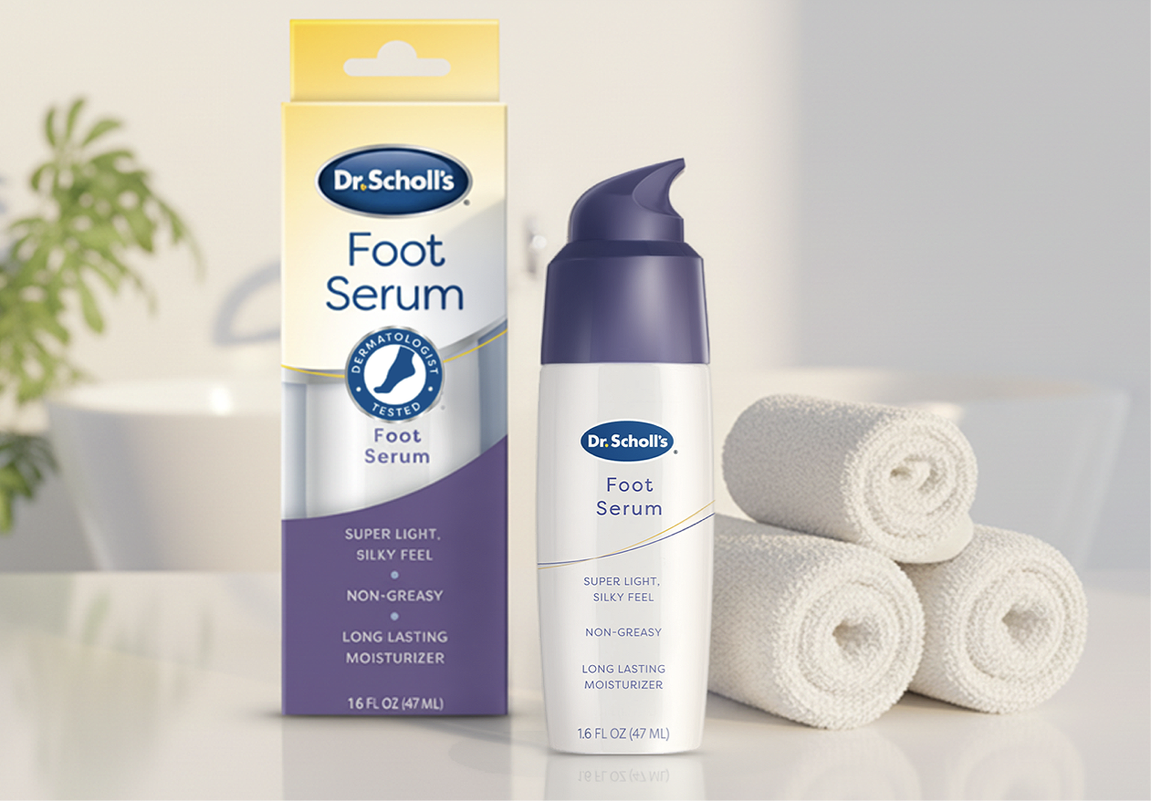 A bottle of Dr. Scholl's Foot Serum next to its packaging box and three rolled white towels on a bathroom or spa setting with a plant in the background.