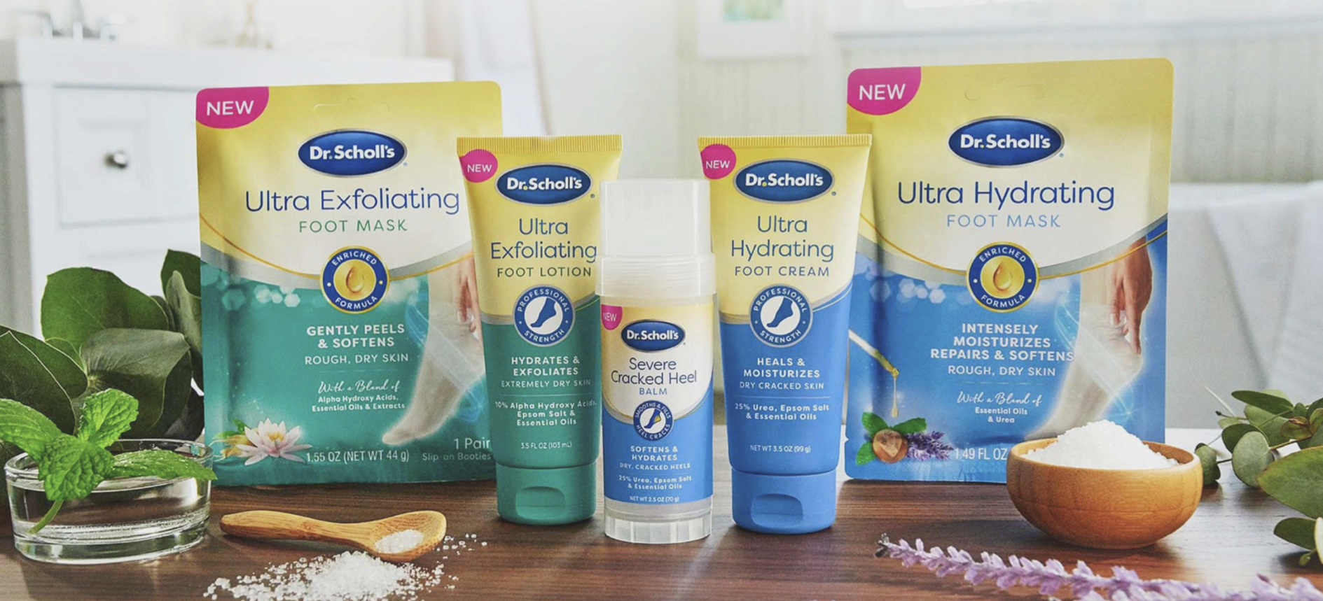 Collection of Dr. Scholl's foot care products including Ultra Exfoliating Foot Mask, Ultra Hydrating Foot Mask, and Severe Cracked Heel Balm, surrounded by natural elements such as mint, lavender, eucalyptus leaves, and a small bowl of salt on a wooden surface.