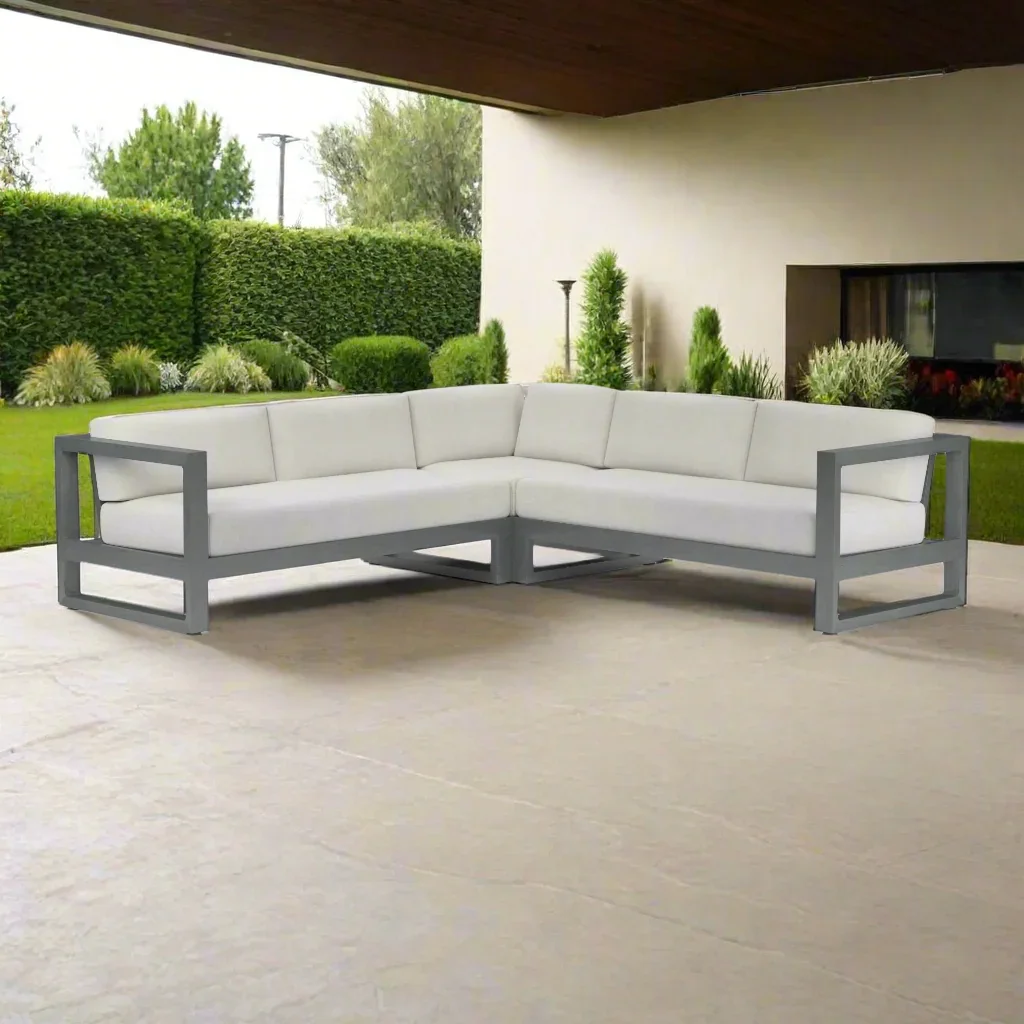 White outdoor sectional sofa on a concrete patio in a backyard with green trees and bushes.