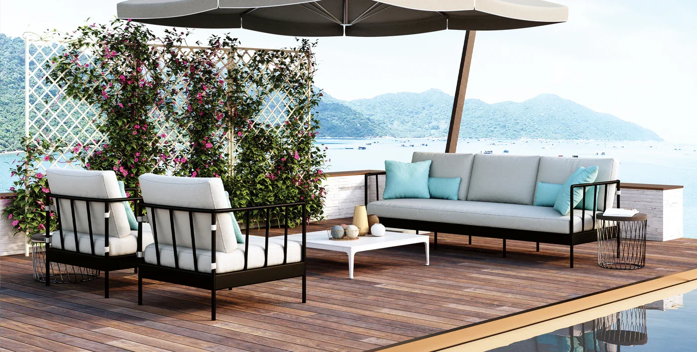 Outdoor patio with white cushioned furniture, teal pillows, a white coffee table, potted plants, and a view of a body of water with mountains in the background.