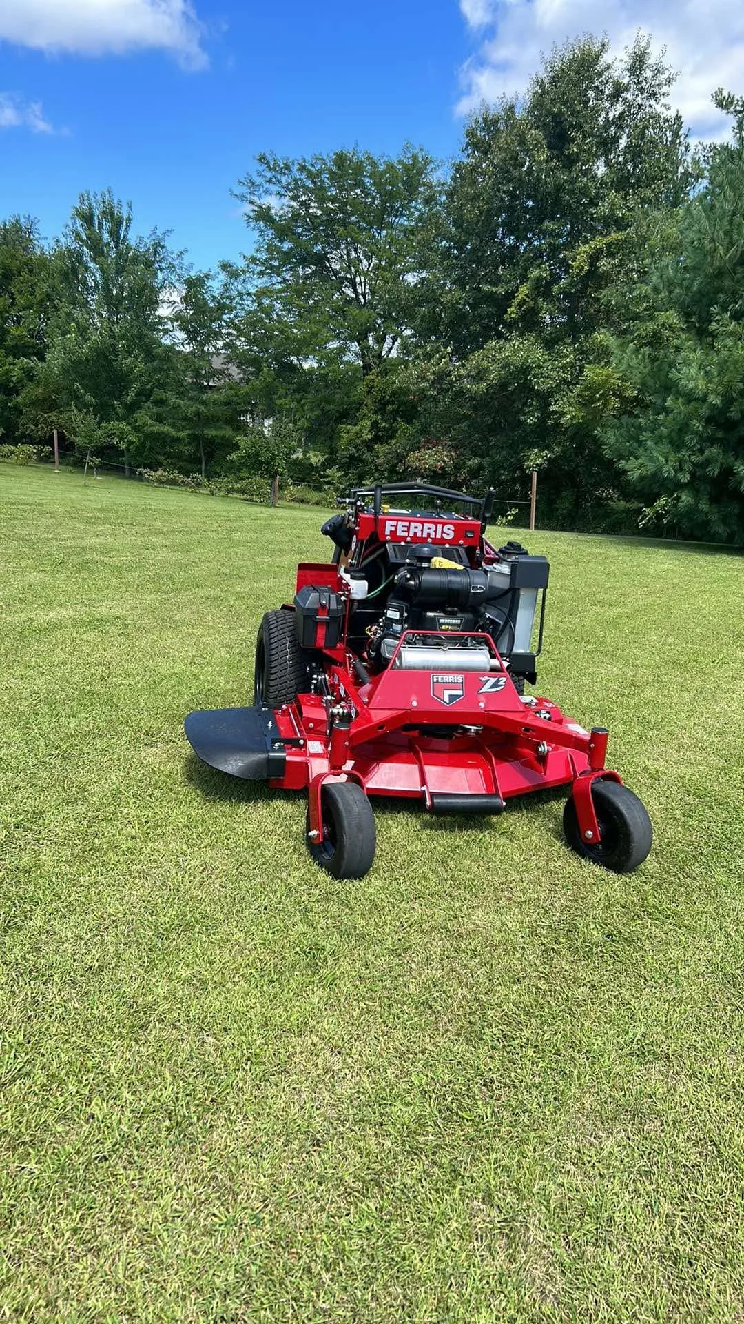 Red Ferris Z2 turf mower on a grassy field with trees and a blue sky in the background.