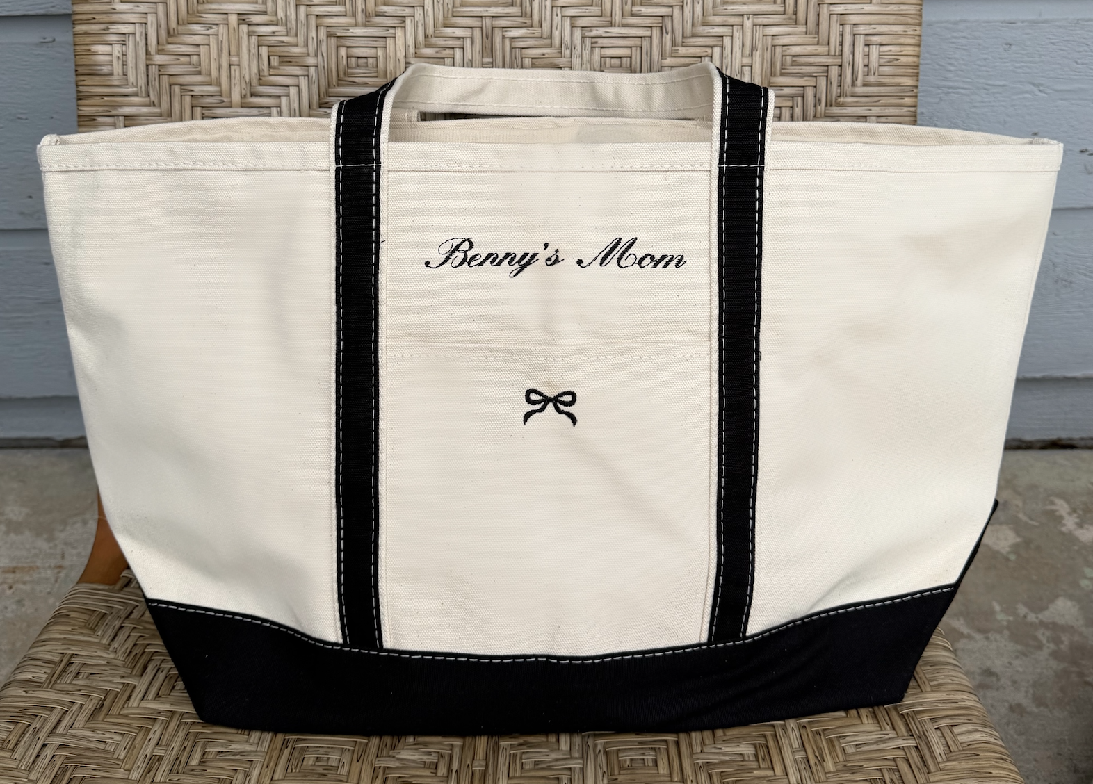 A large canvas tote bag with black handles and embroidery that reads "Benny's Mom" and a small bow. 