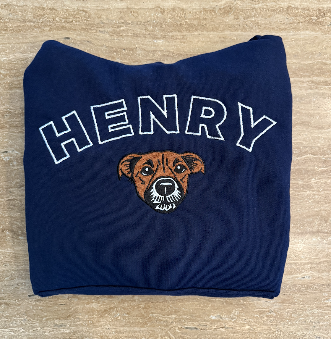 A navy blue sweatshirt with an embroidered dog's face and the name 'HENRY' above it.