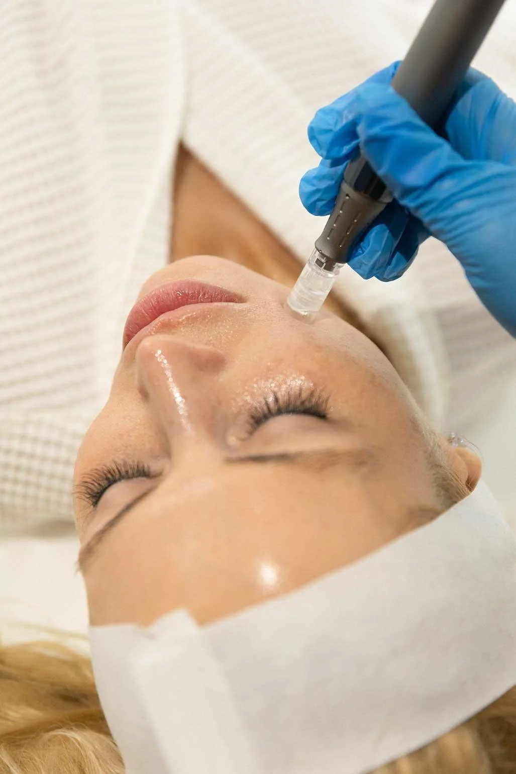 Overhead close-up of a gloved esthetician applying a nano infusion pen to a client's cheek during a nano infusion facial treatment at Lunar Ambitions in Orlando FL.