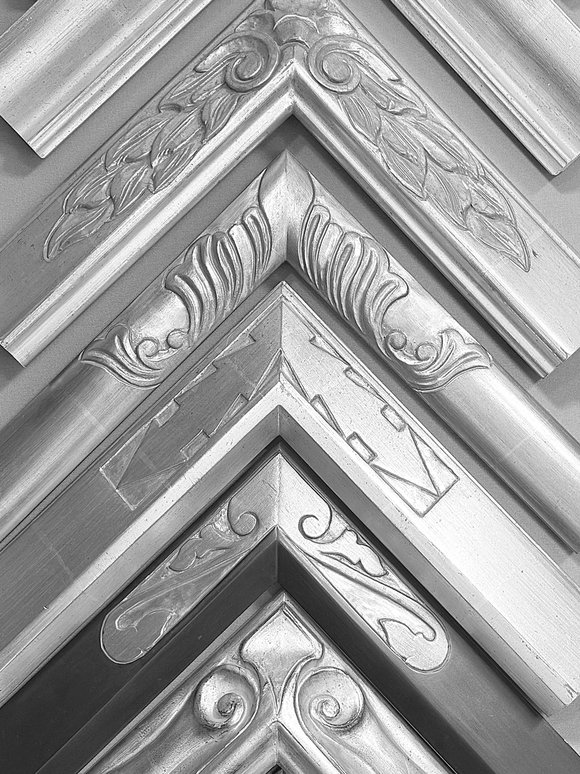 Black and white close-up photo of ornate decorative corner moldings with floral and scroll patterns.