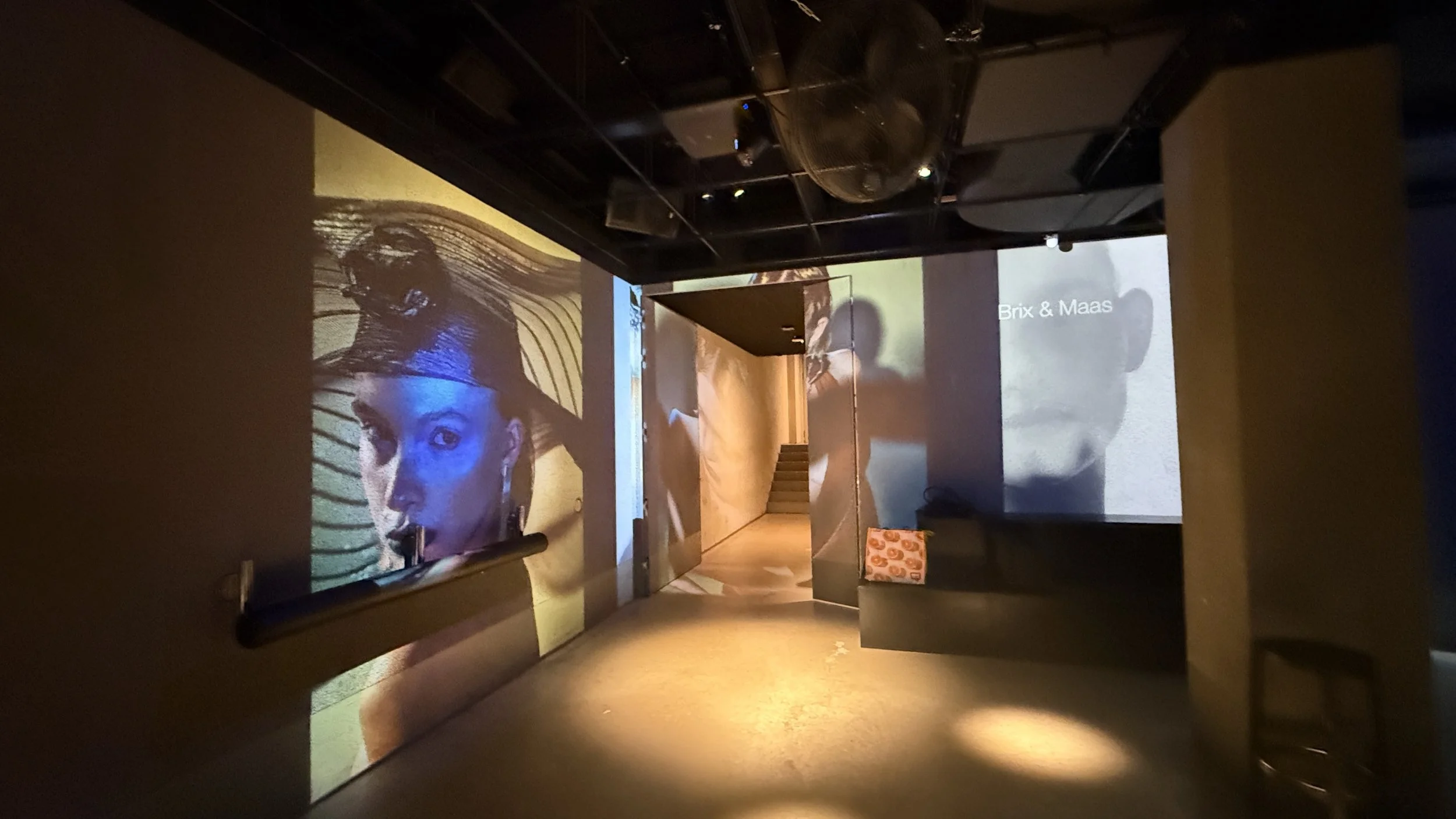 A dark room with multiple projection screens showing images and text, including a woman's face and the words 'Brix & Maas'.