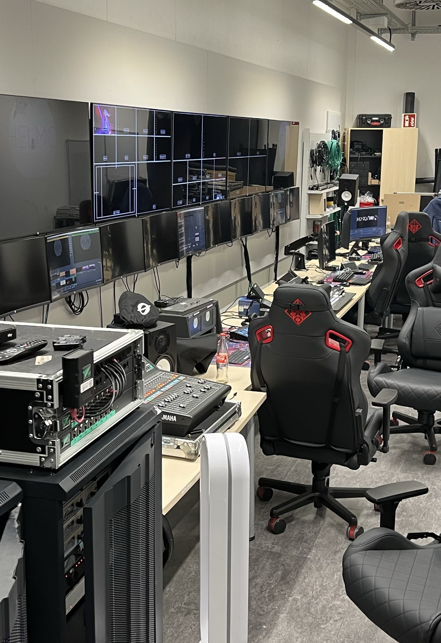 Multiple monitors, gaming chairs, and electronic equipment in an office or control room.