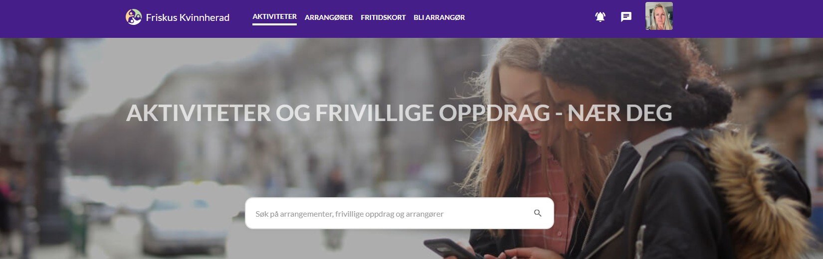 To kvinner med jakker ser på en mobil, utendørs i byen.