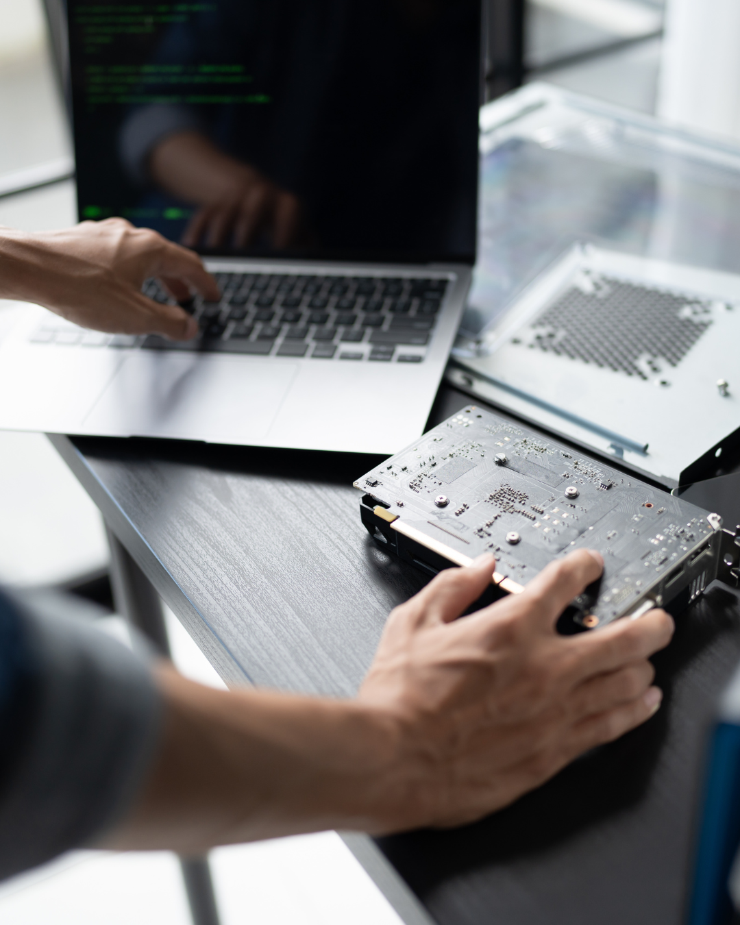 Person working on repairing or assembling a hard drive with a laptop and electronic components on a work desk.