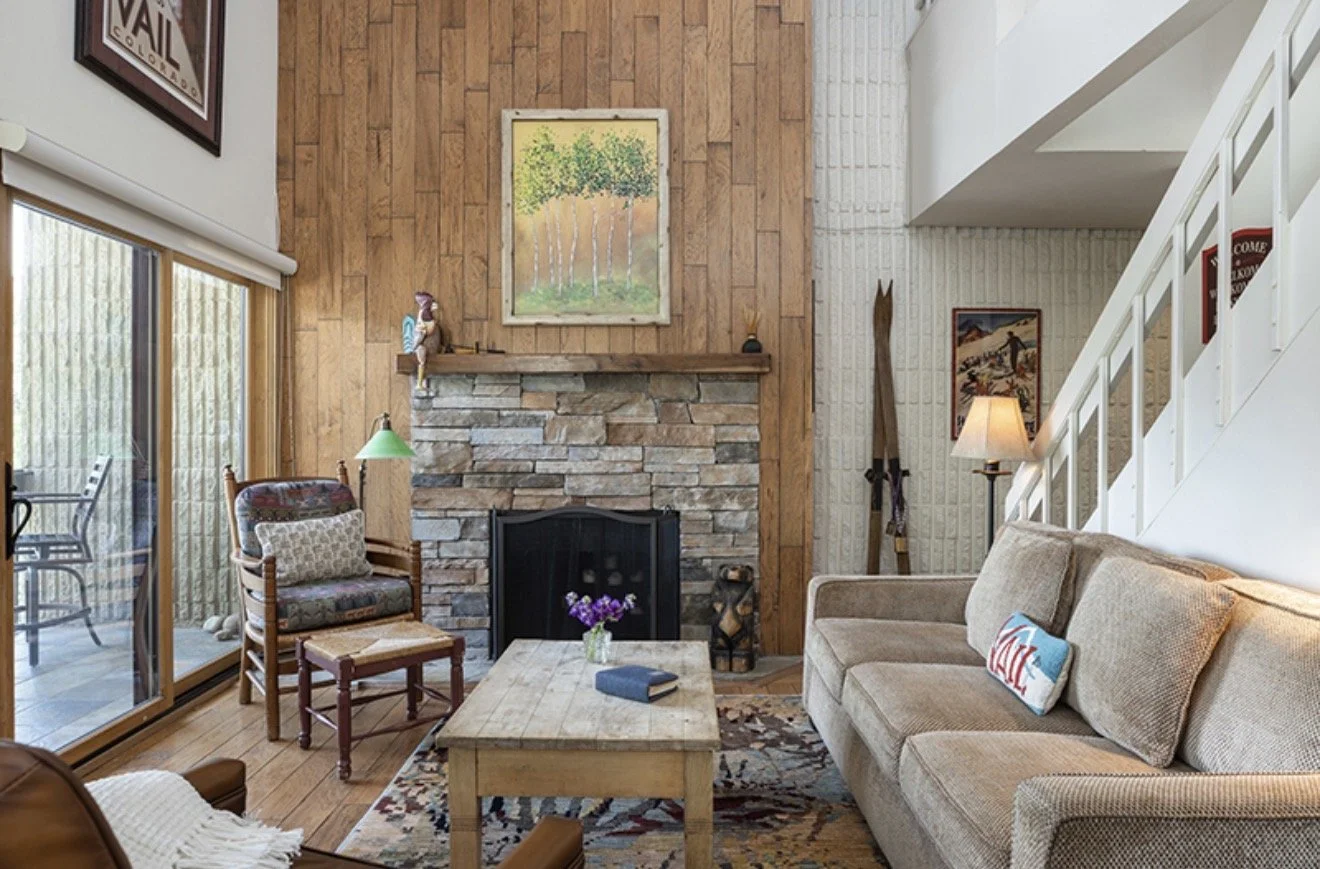 Living room with a brick fireplace, wooden wall, beige couch, wooden coffee table, armchair, and sliding glass door leading to an outdoor patio.