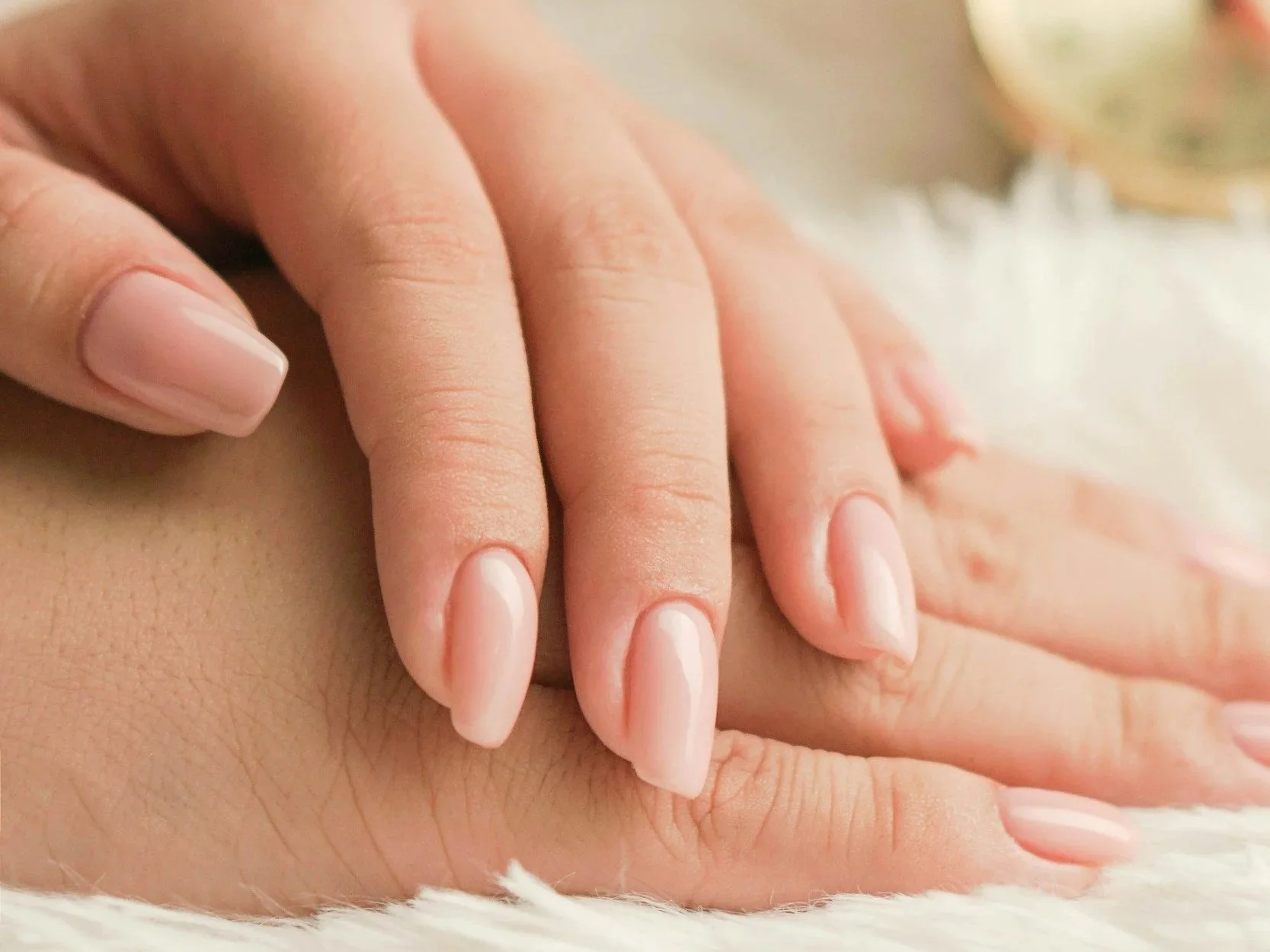 Close-up of a person's hand resting on another person's hand, with manicured nails and soft lighting.