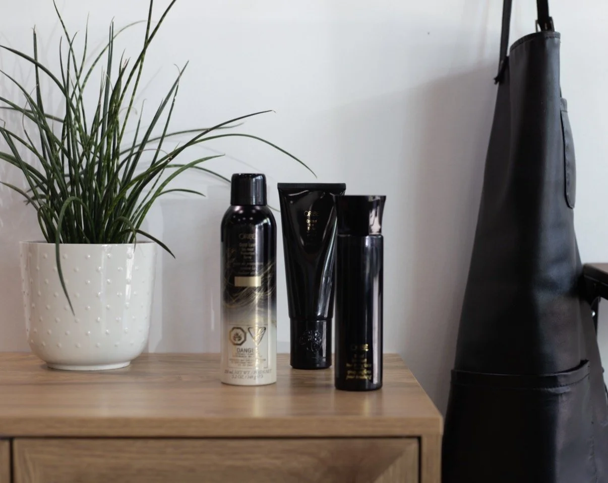 White pot with green plant on wooden surface, next to black bottles and tubes, with a black bag in the background.