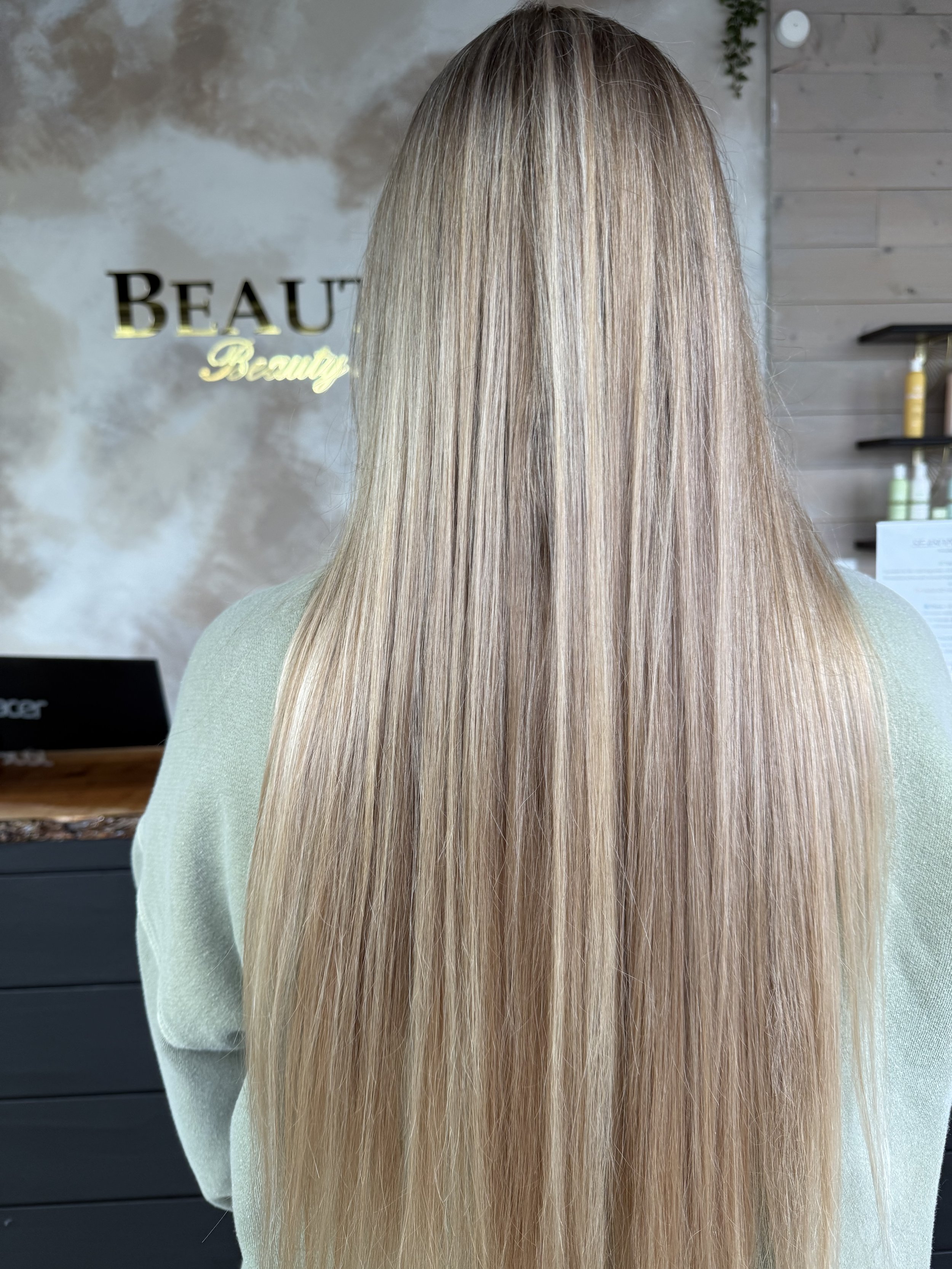 Back of a person's head with long, straight, blonde hair in a salon setting.
