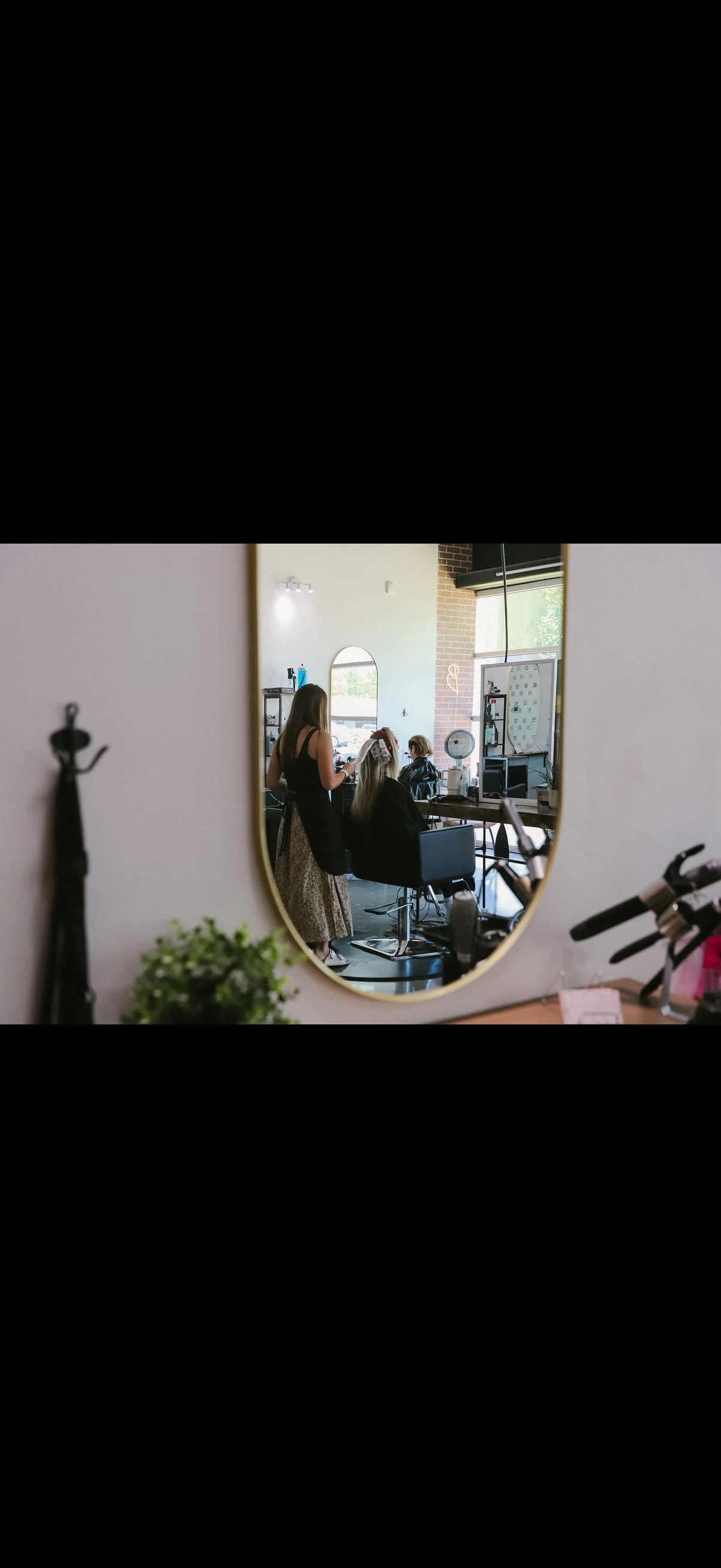 Salon scene with a stylist working on a client's hair, viewed through a mirror in a modern hair salon.