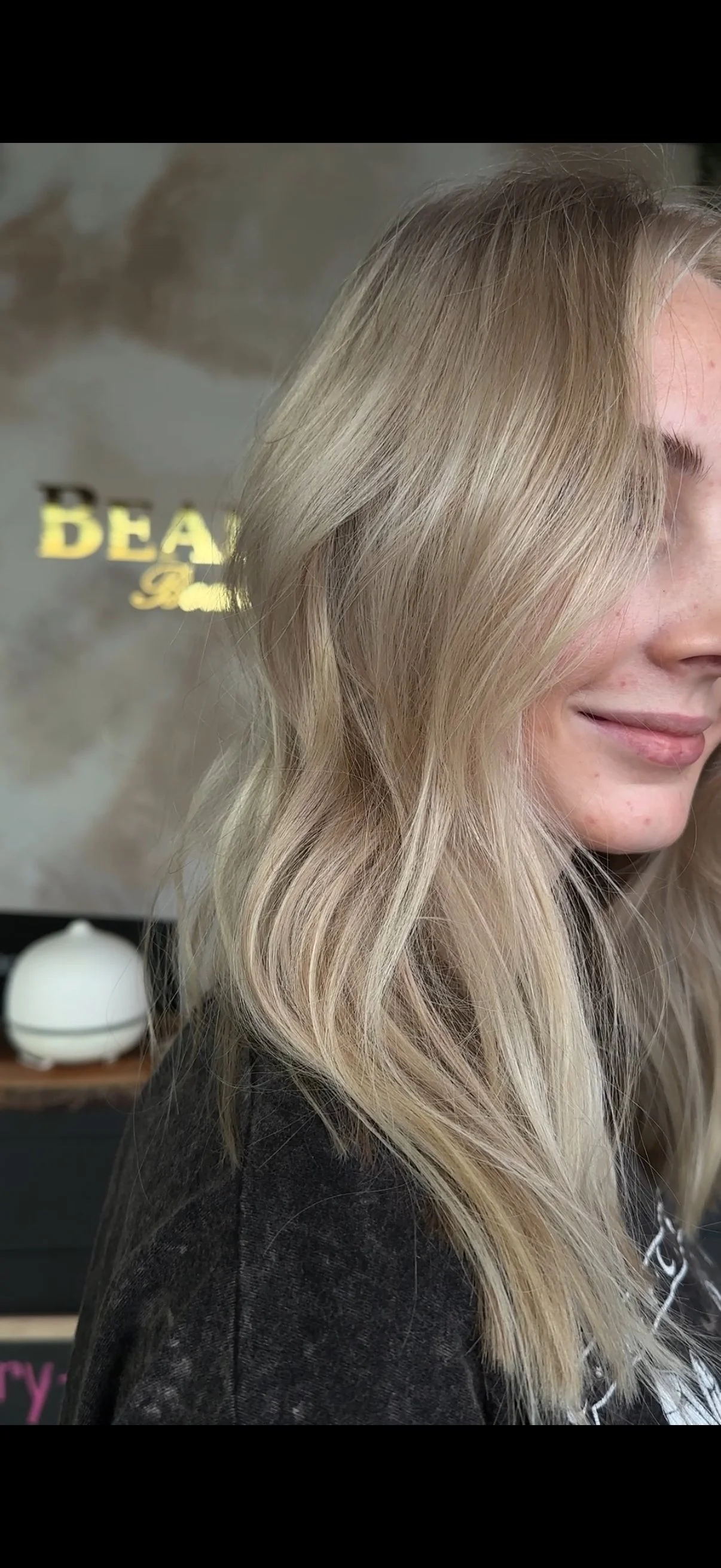 Close-up of a woman's side profile with wavy, blonde hair and a smiling expression.