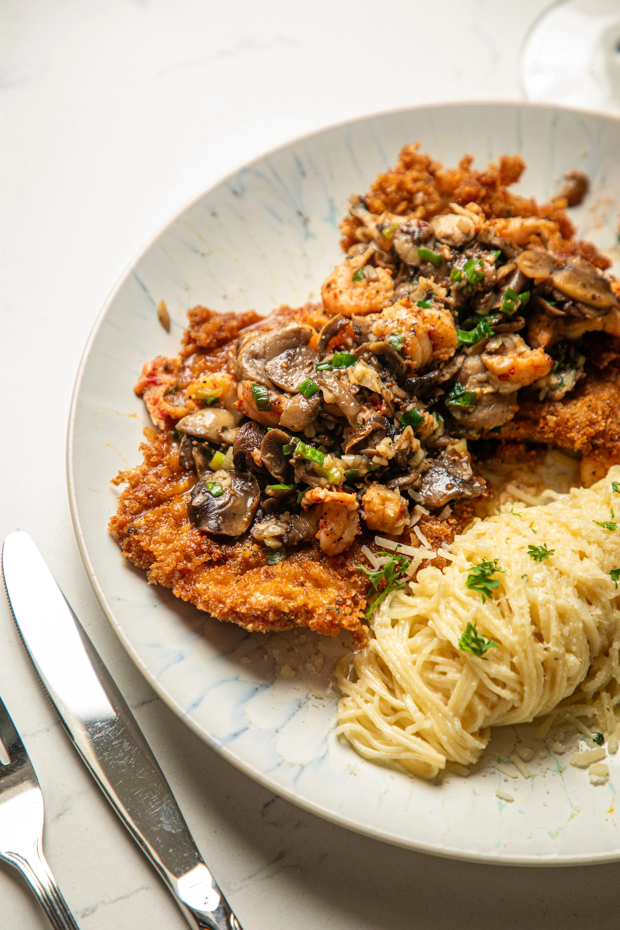 Breaded chicken fried steak topped with sautéed mushrooms and green onions, served with a side of creamy garlic pasta.