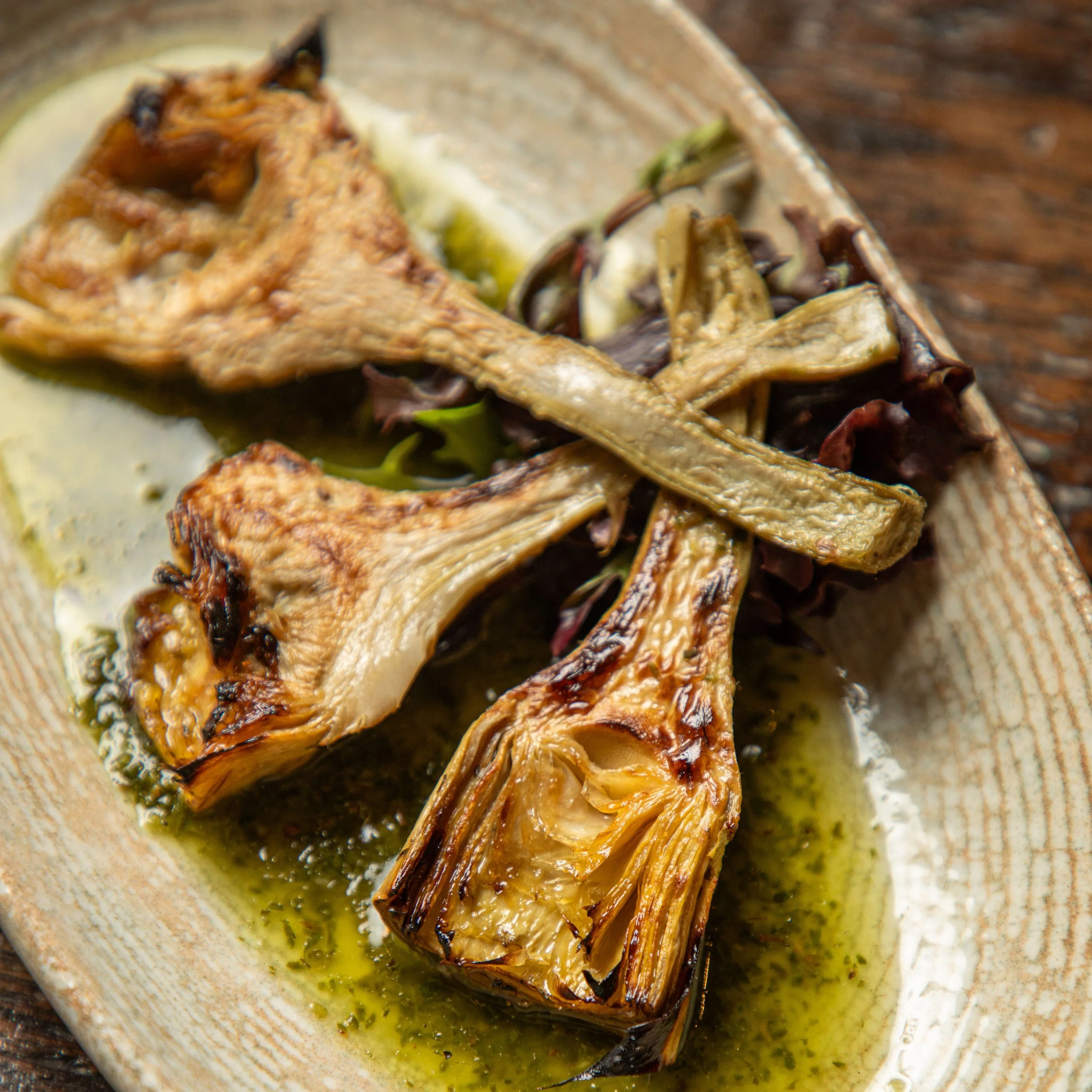 Grilled artichoke hearts served on a ceramic plate with green herb sauce.