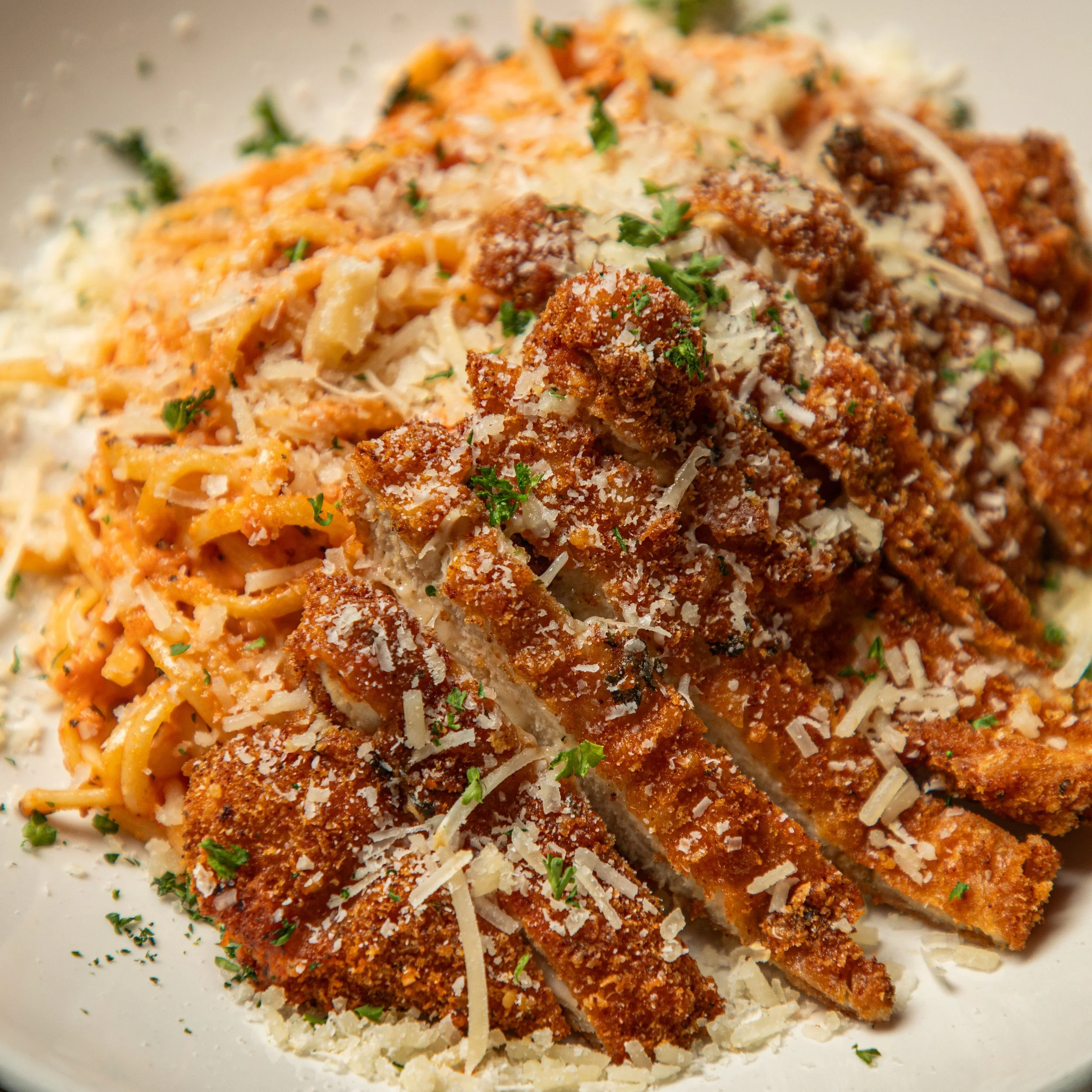 A plate of breaded and fried chicken cutlets topped with shredded cheese and parsley, served with pasta.
