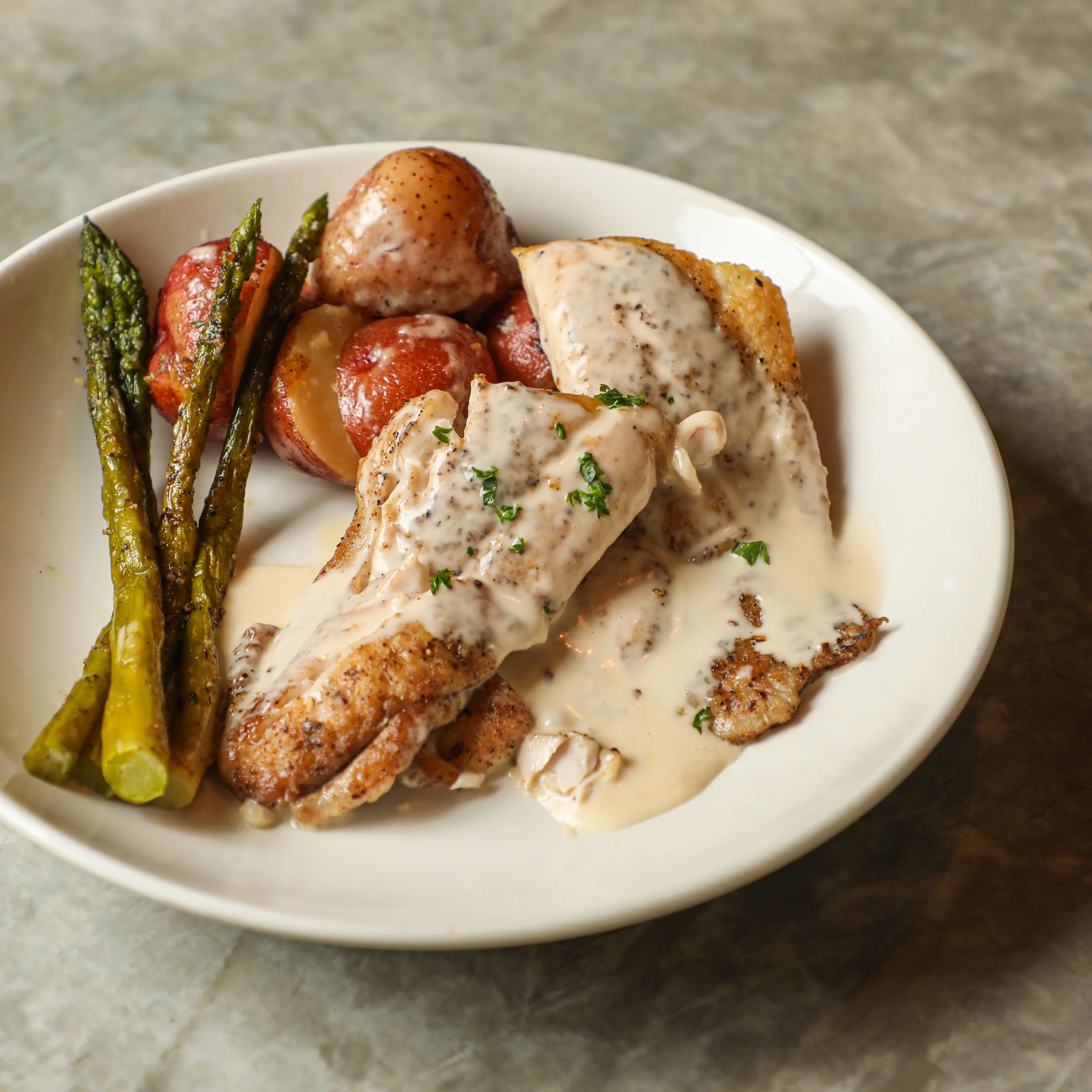Plate with Gulf Seafood covered in creamy mushroom sauce, roasted red potatoes, and asparagus spears.