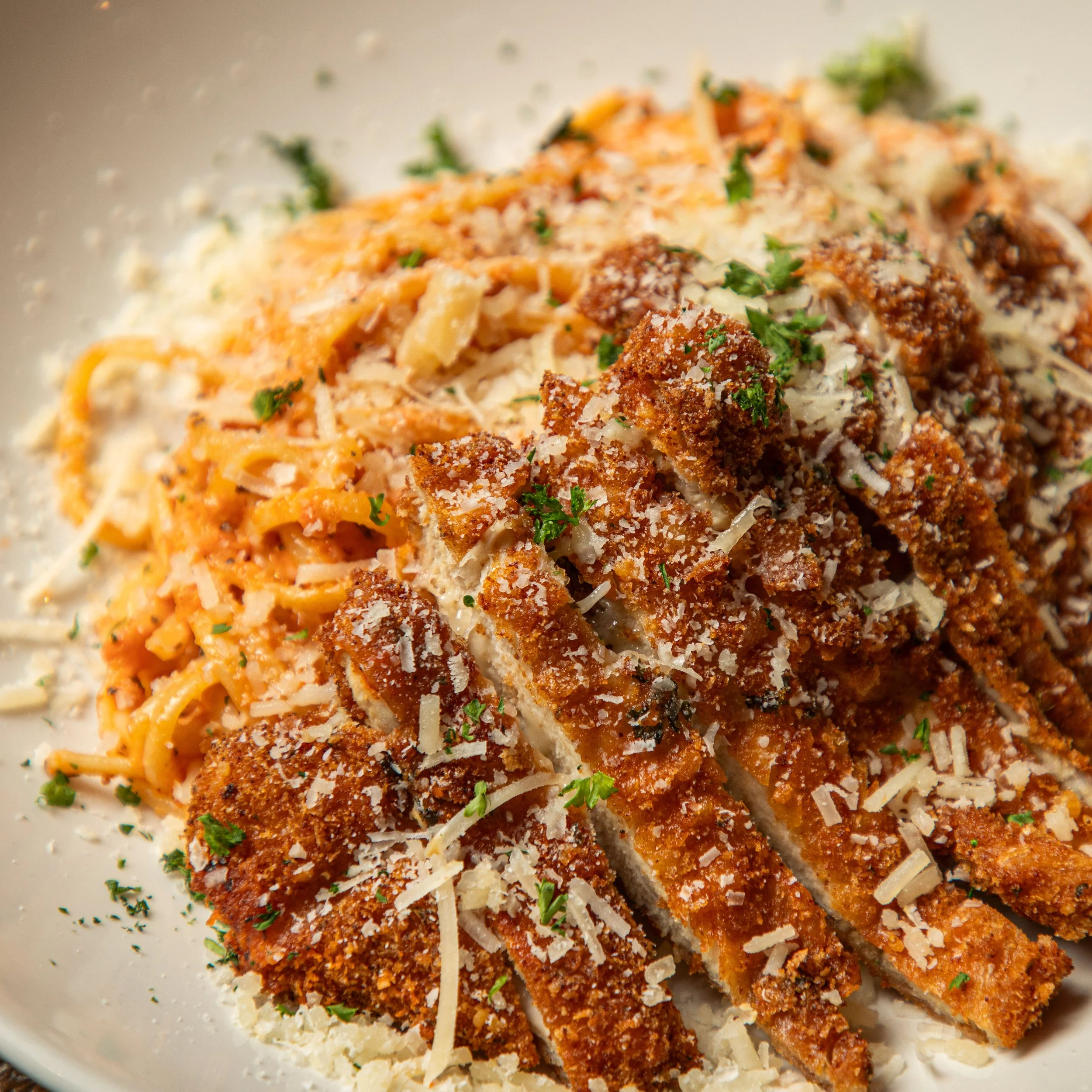 Close-up of breaded and fried chicken served over pasta with Parmesan cheese and parsley garnish.