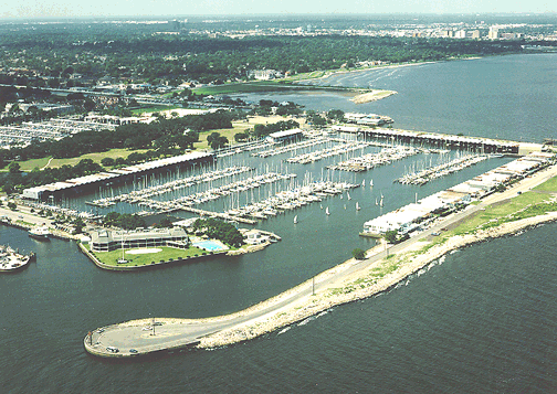 Aerial view of West End marina with numerous boat slips and a breakwater, adjacent to a body of water and a shoreline with greenery.