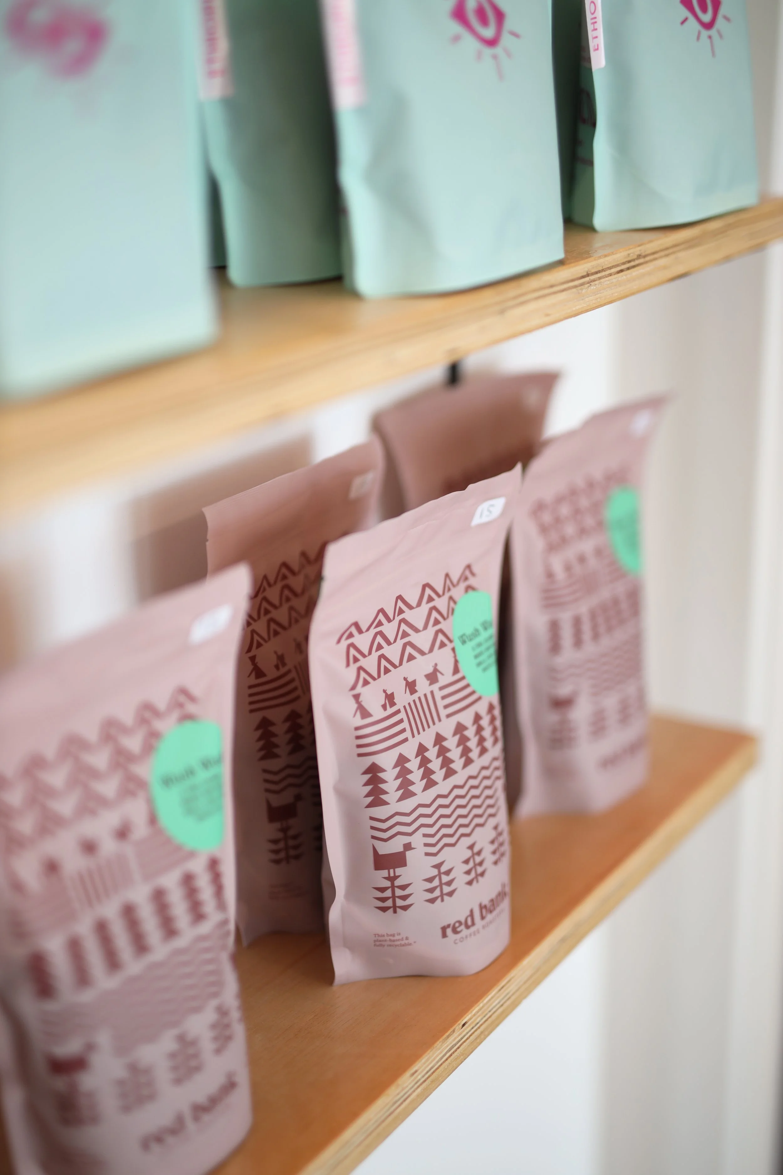 Close-up of pink coffee bags with brown designs on a wooden shelf.