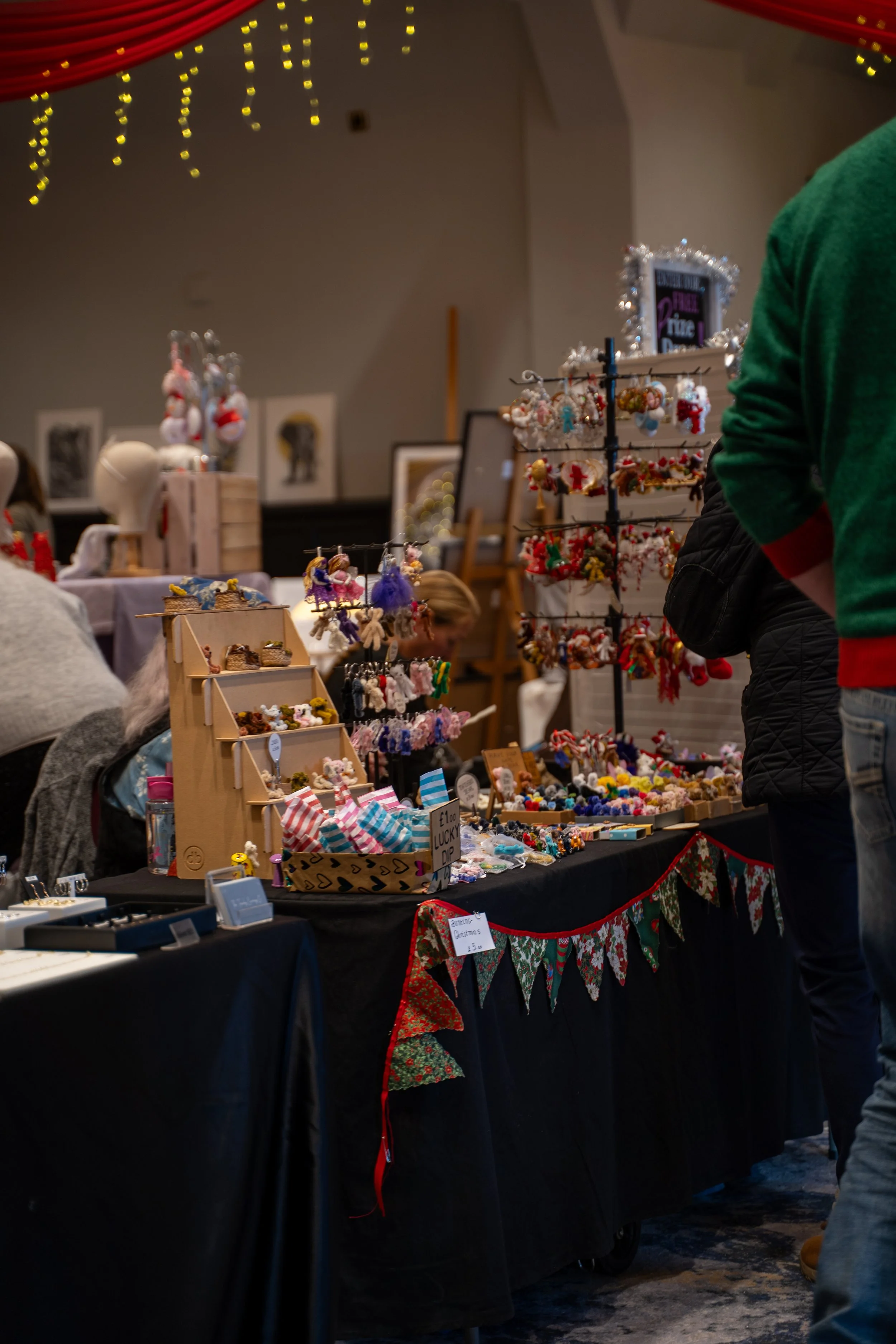 Indoor jewelry market stall decorated with Christmas-themed jewelry and accessories, with people browsing, and festive decorations hanging from the ceiling.