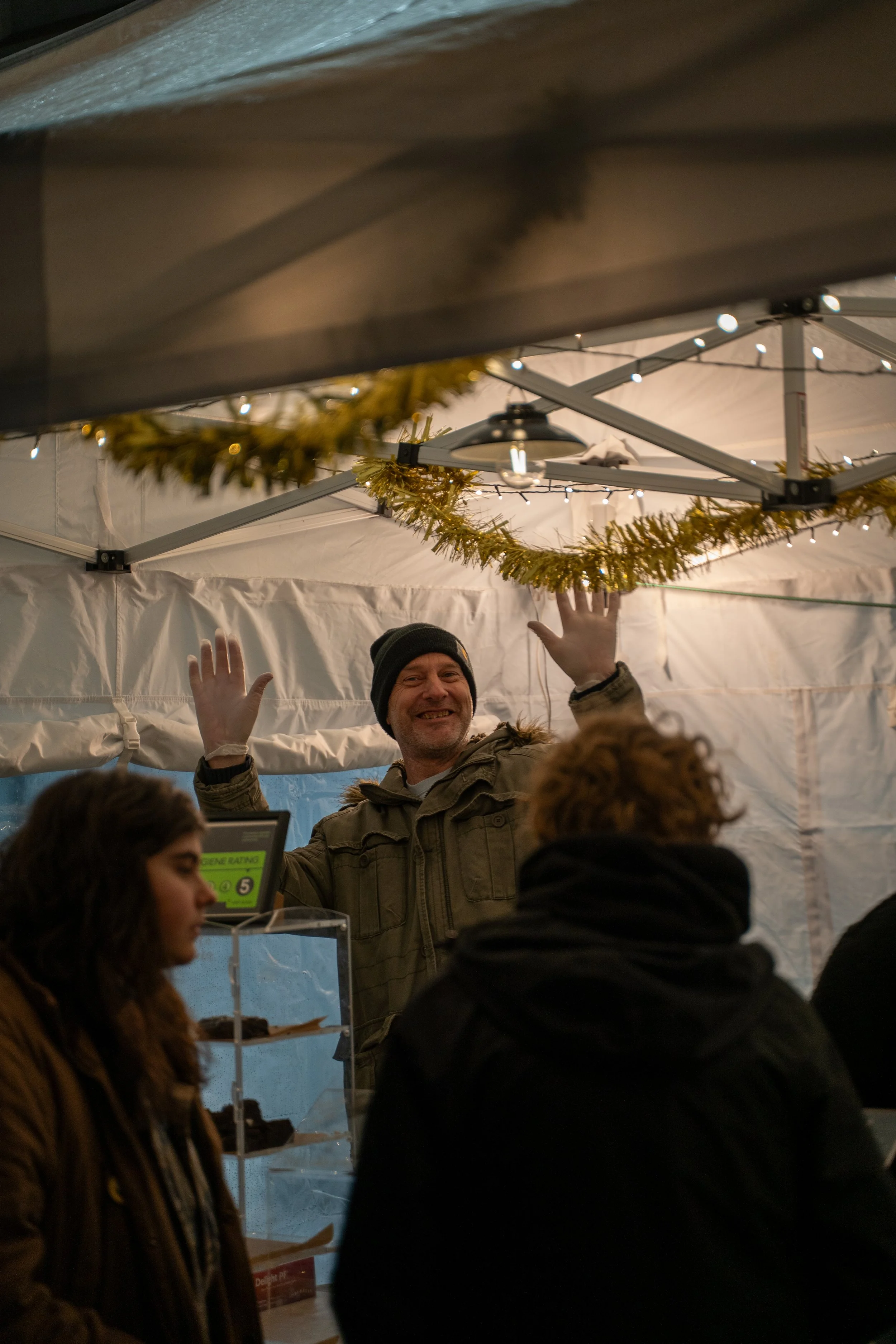 People inside a festive tent with holiday decorations, including gold tinsel garlands and string lights, engaged in a cheerful event or gathering.