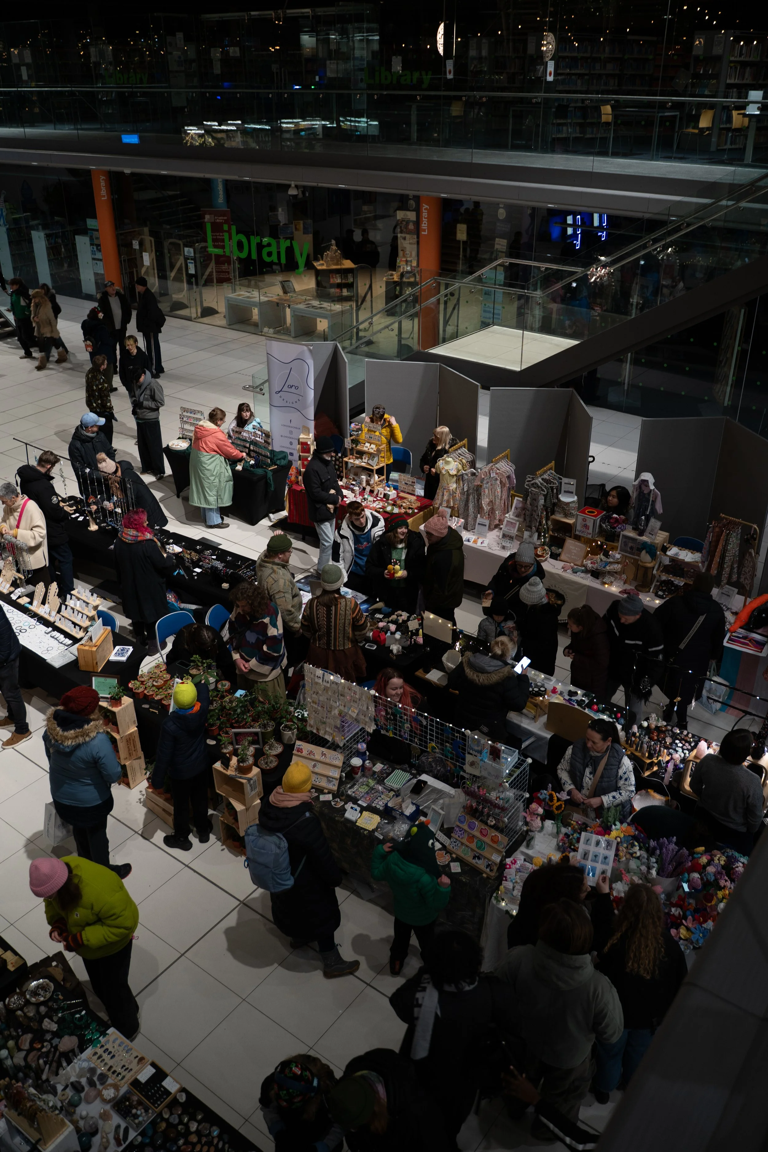 People shopping at booths inside a shopping mall with a second level in the background.