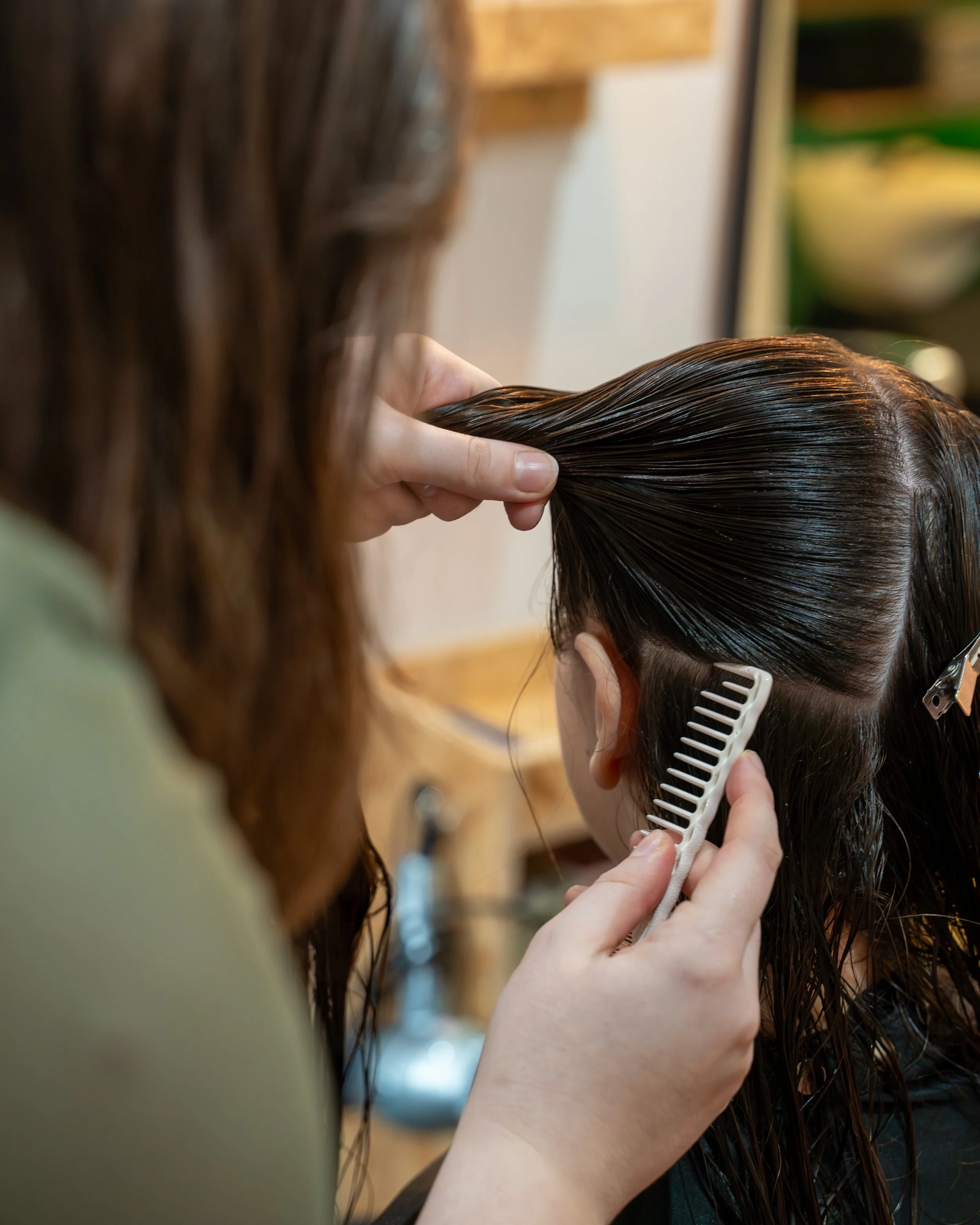 A hairstylist using a comb and fingers to section and style the wet, dark brown hair of a client.