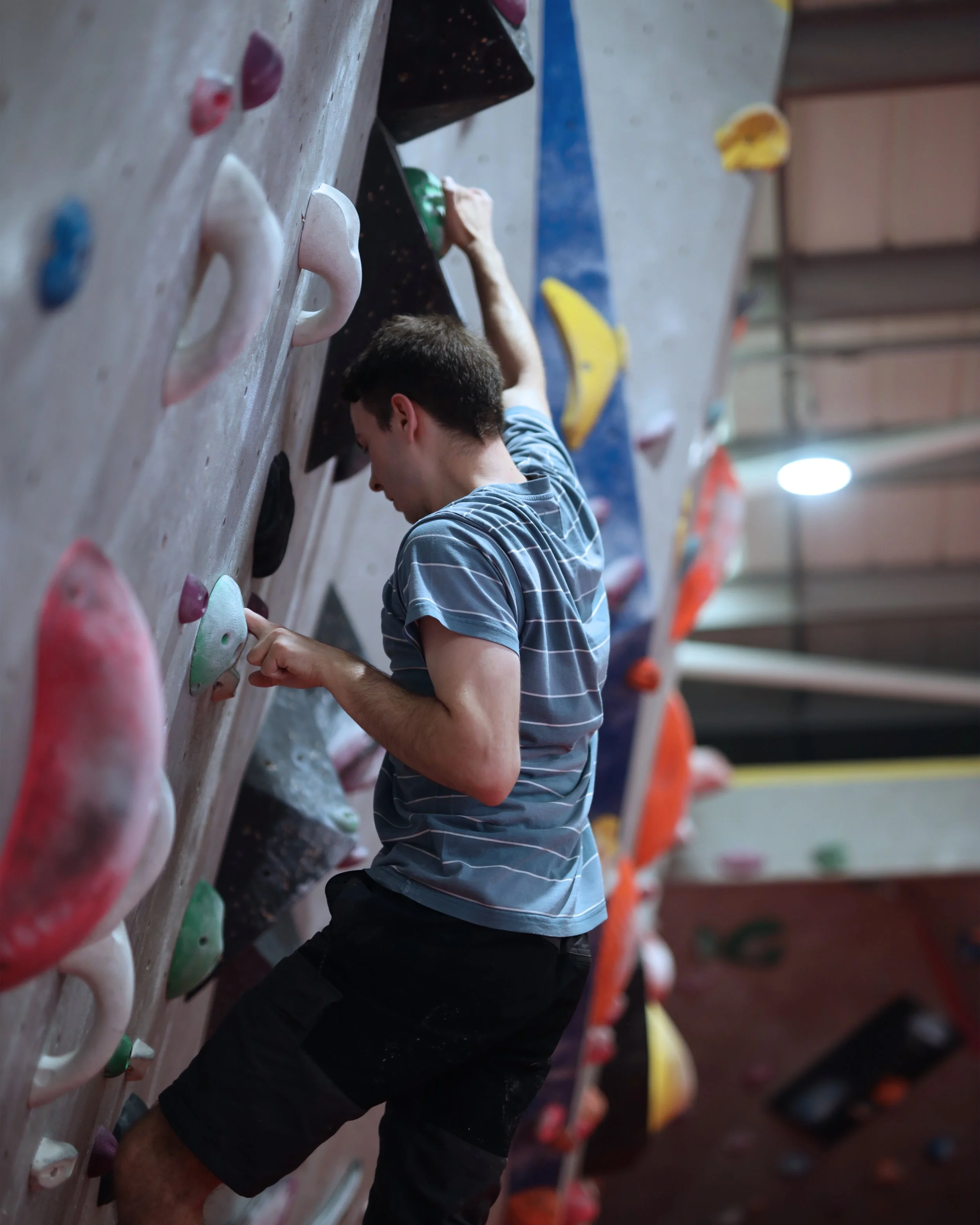 A young man climbing an indoor rock climbing wall with colorful holds.