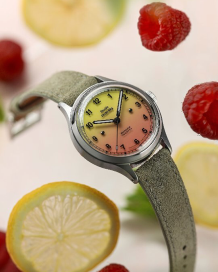 Wristwatch with a beige band and yellow and orange face surrounded by raspberries and lemon slices.