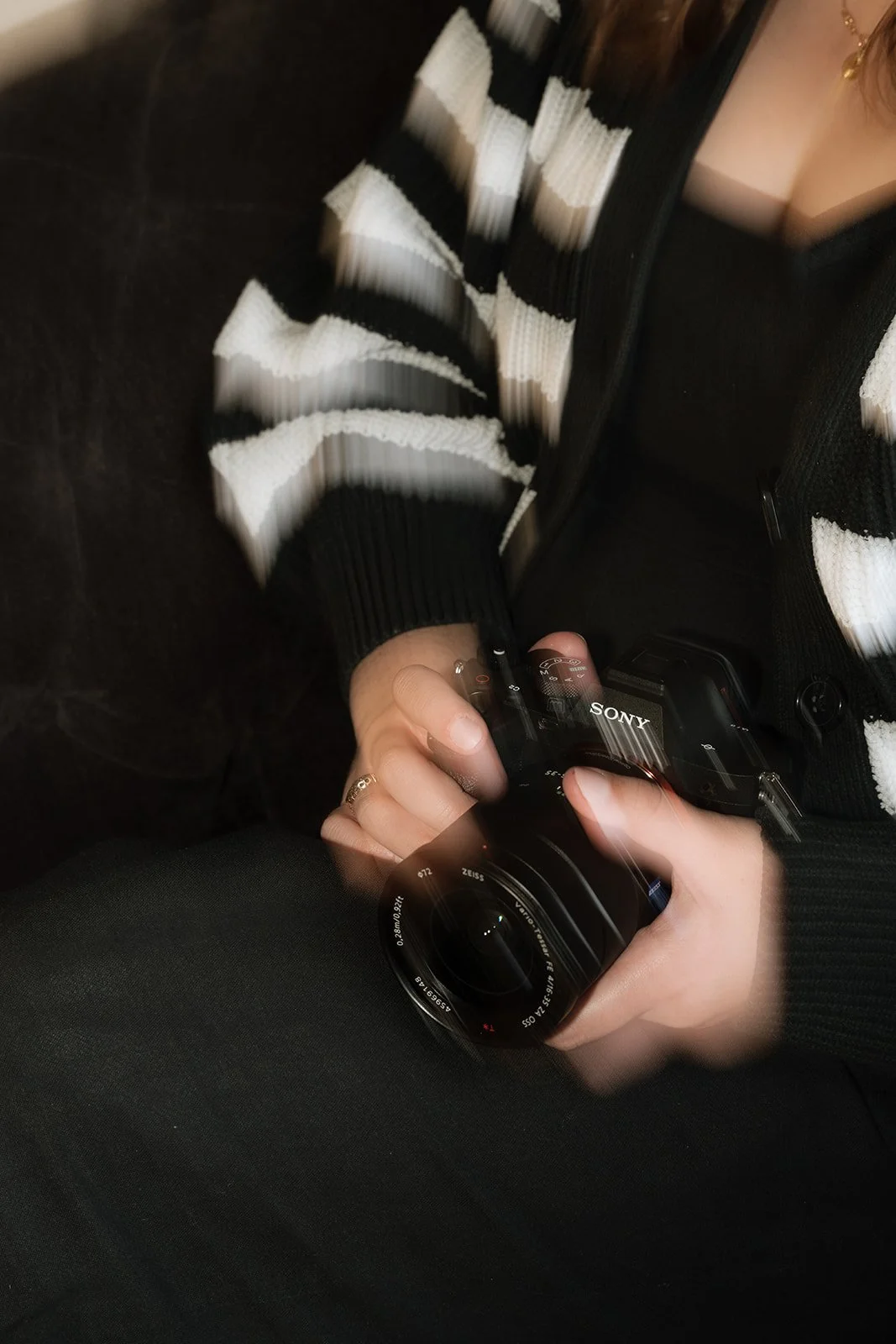 A person holding a Sony camera, wearing a black and white striped sweater and black pants.