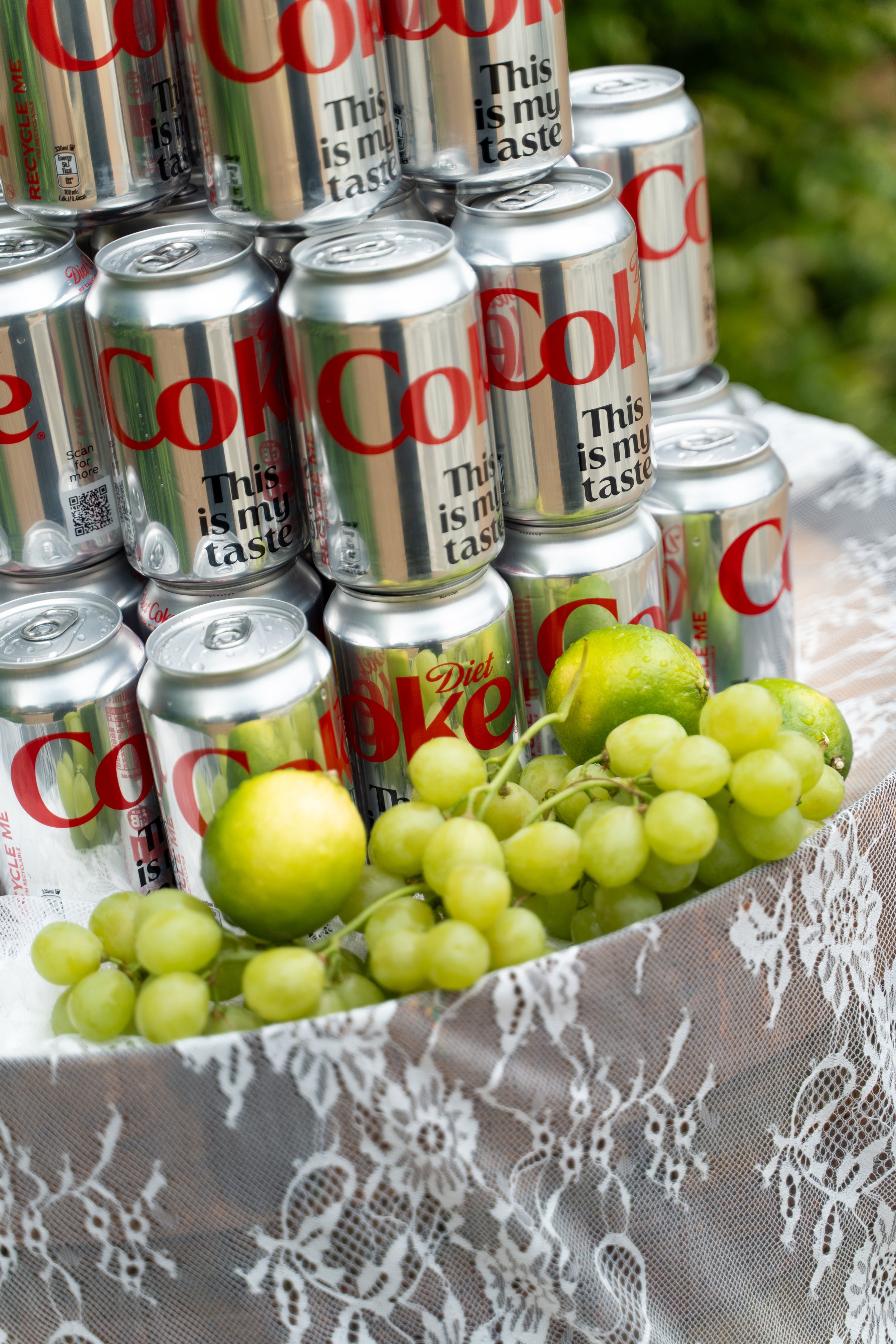 Cans of Diet Coke and grapes on a lace tablecloth.