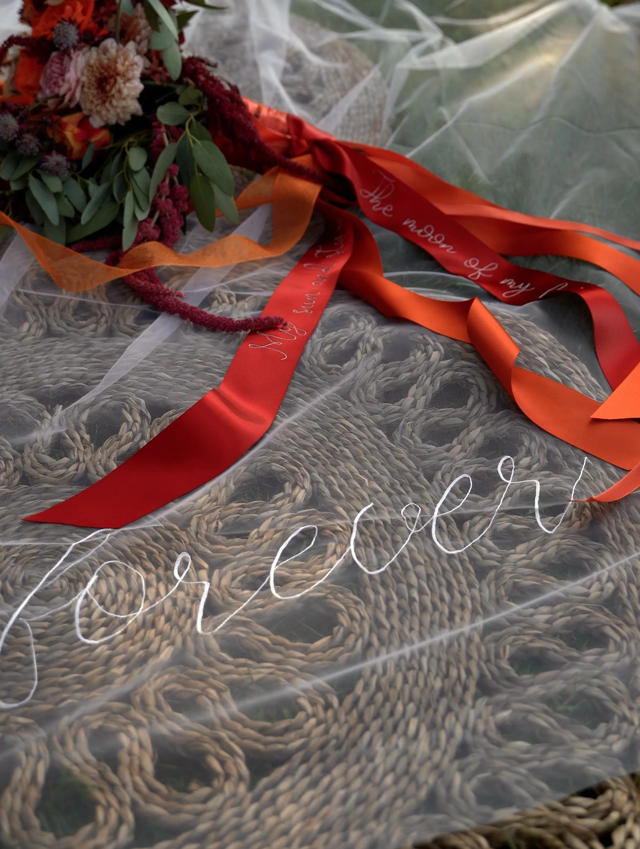 A colorful flower bouquet with orange and red ribbons, placed on a textured gray surface covered with a transparent plastic sheet.