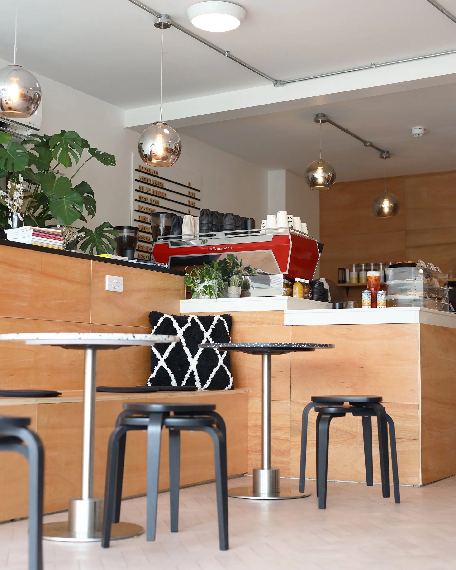 Interior of a coffee shop with small tables and chairs, a counter with cups and coffee supplies, and a menu on the wall.