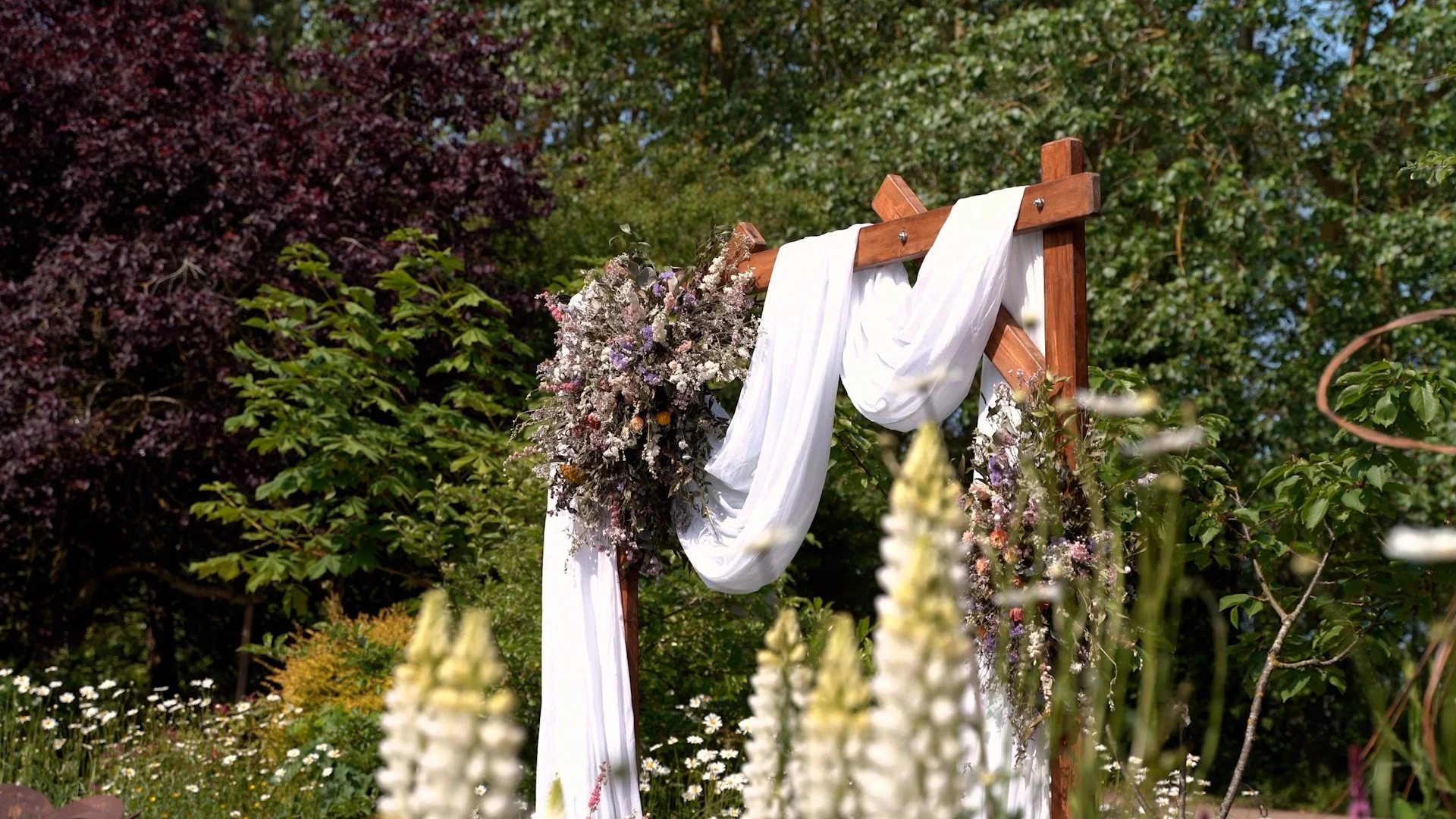 Wedding arch decorated with flowers and white fabric in an outdoor garden setting.