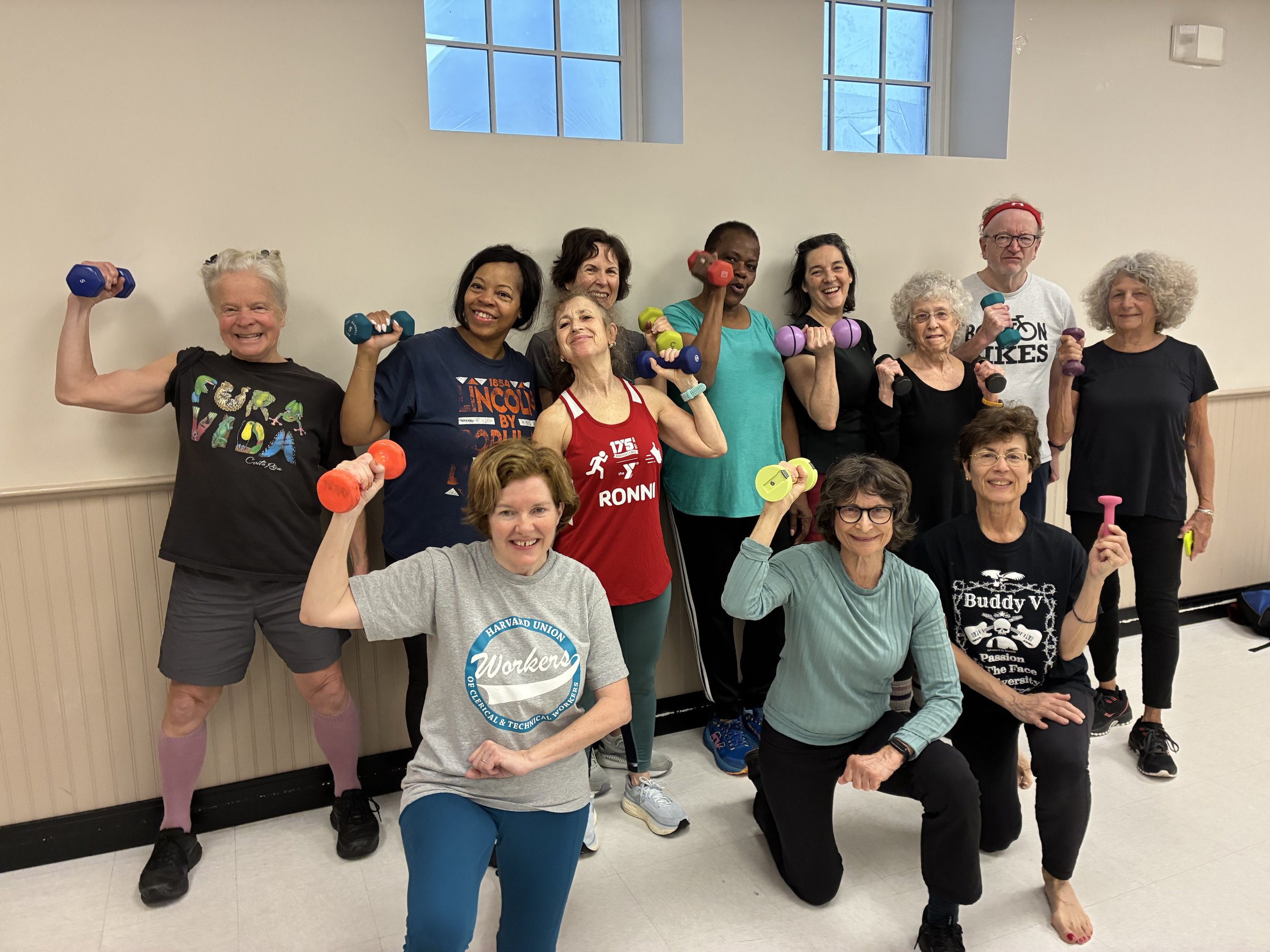 A group of diverse elderly women and men exercising with small dumbbells in a fitness class indoors, smiling and showing strength.