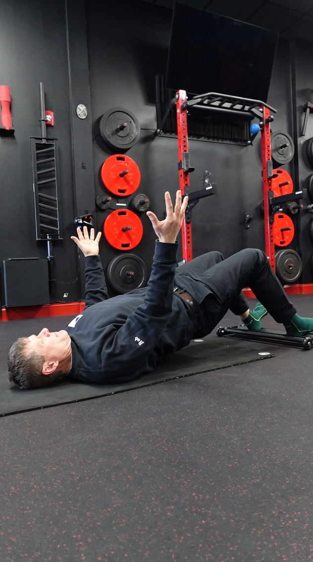 Rob Skinner doing Roller Hamstring Curls on the gym floor, surrounded by workout equipment and weight plates.