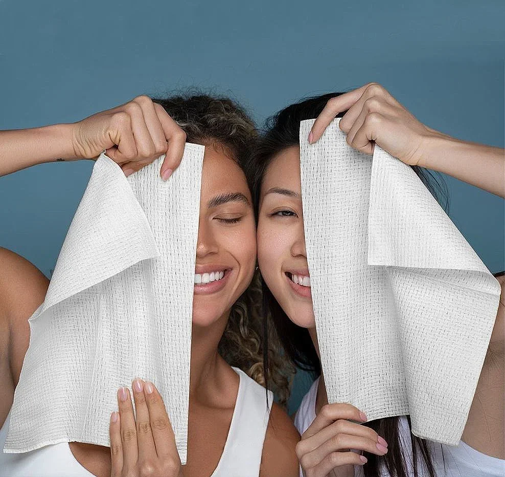 Two women smiling and holding white paper towels in front of their faces, playfully hiding half of their faces.