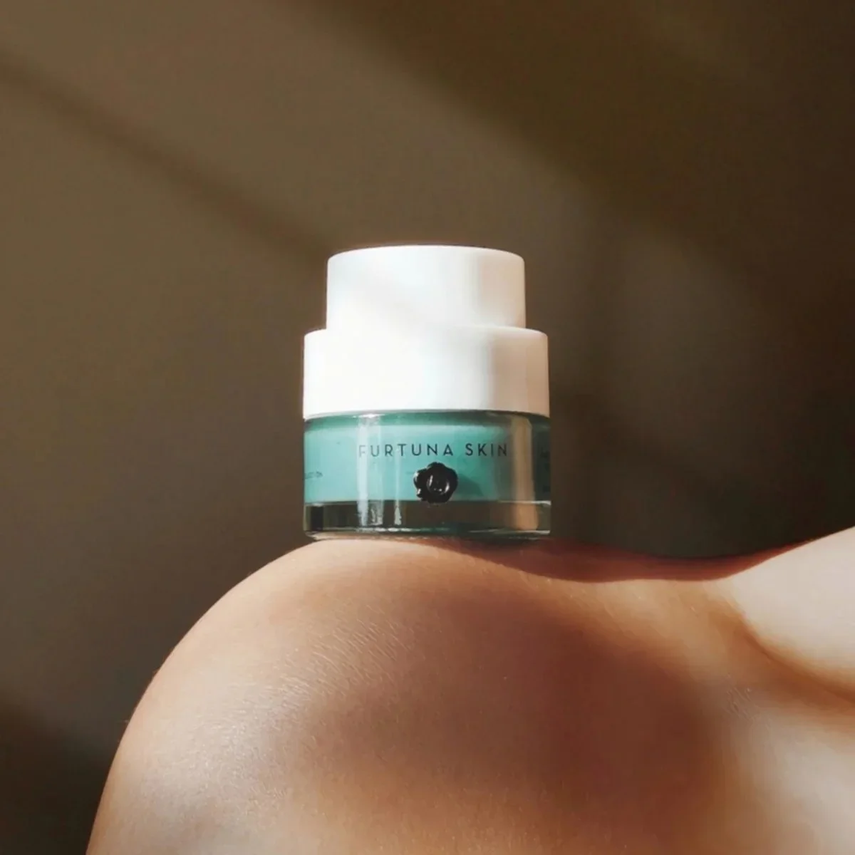 A small jar of Furtuna Skin skincare product balanced on a person's knee in natural light.